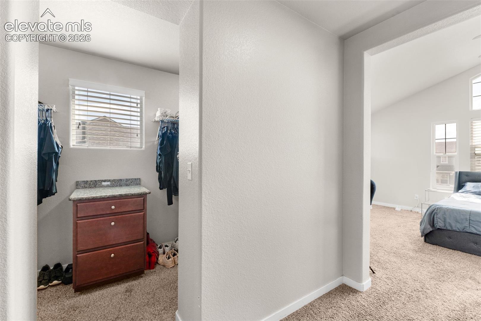 Walk-in storage area featuring built-in cabinetry with stone-finish countertop, carpeted flooring, and a window with horizontal blinds