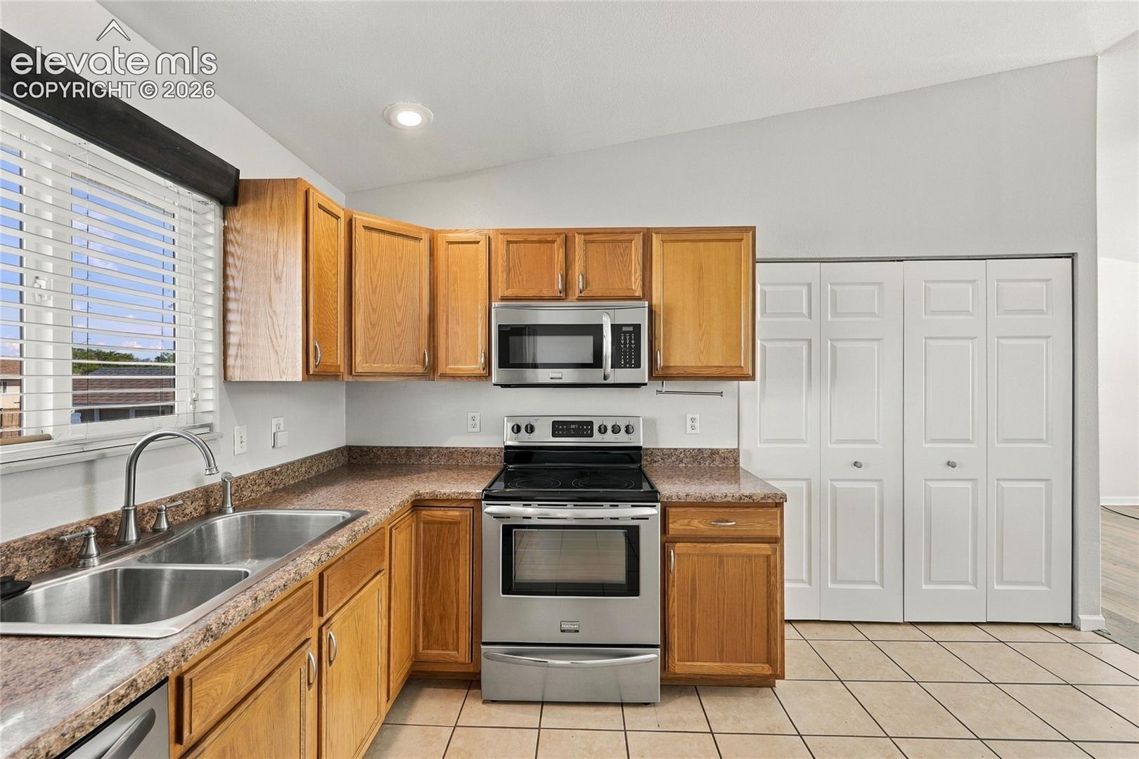 Kitchen featuring wood cabinetry, stone-finish countertops, stainless steel appliances, double-basin undermount sink, and tiled flooring