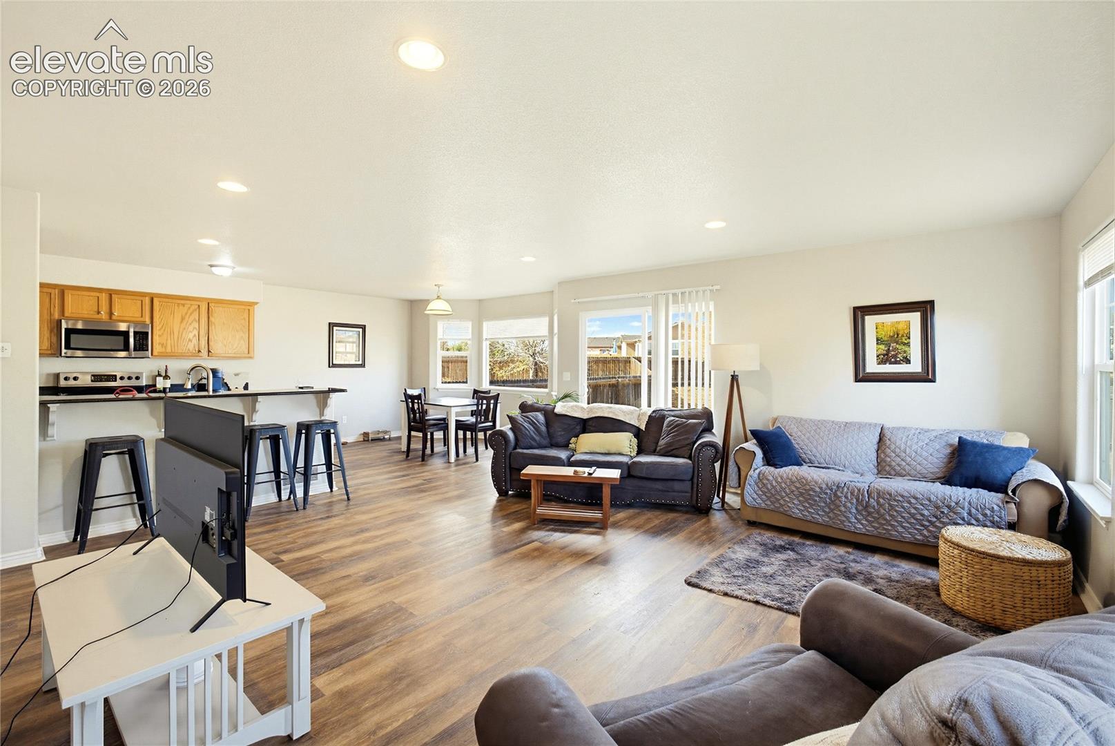 Open-concept living space featuring wood-finish flooring, recessed lighting, a breakfast bar with stone-surfaced countertop, and sliding glass doors