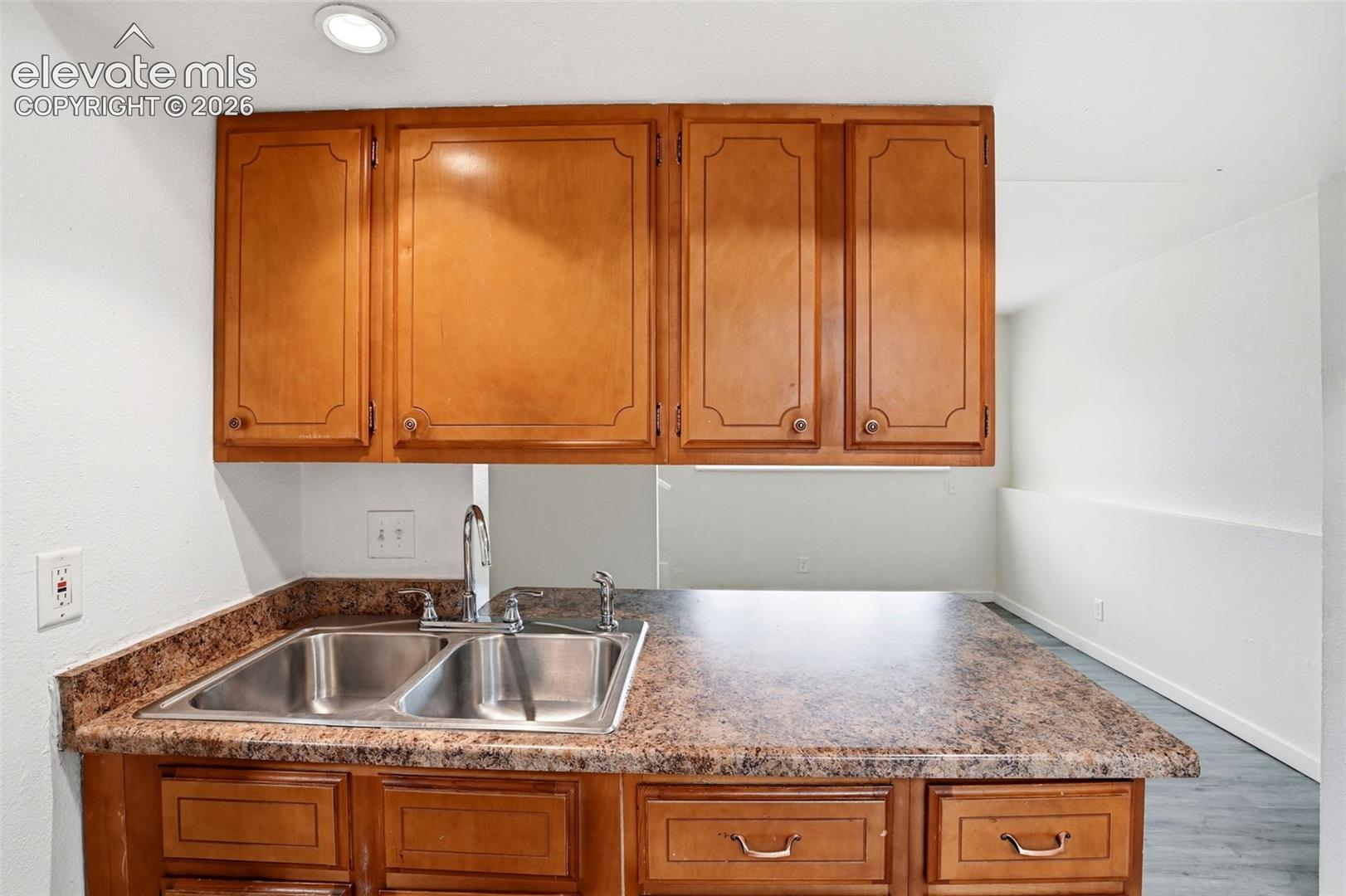 Wood-finish cabinetry with decorative panels, double basin stainless steel sink with a chrome faucet, and a stone-finish countertop