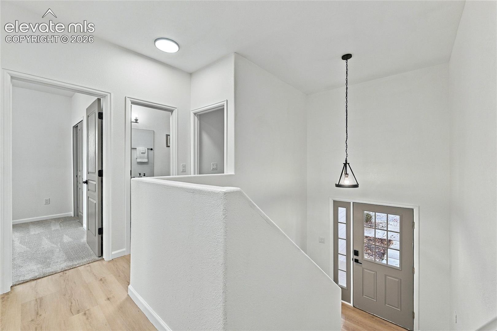Interior landing featuring wood-finish flooring, a pendant light fixture with a geometric frame, a solid core door with glass panels and sidelight, and textured half-wall millwork