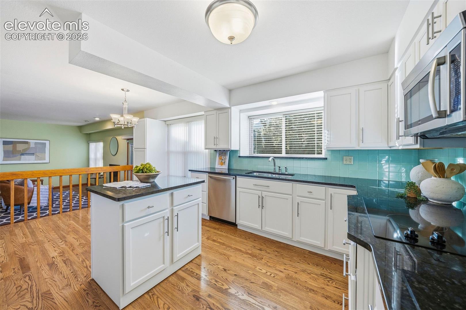 Kitchen featuring white cabinetry, dark stone countertops, wood-finish flooring, a central island, and a stainless steel over-the-range microwave