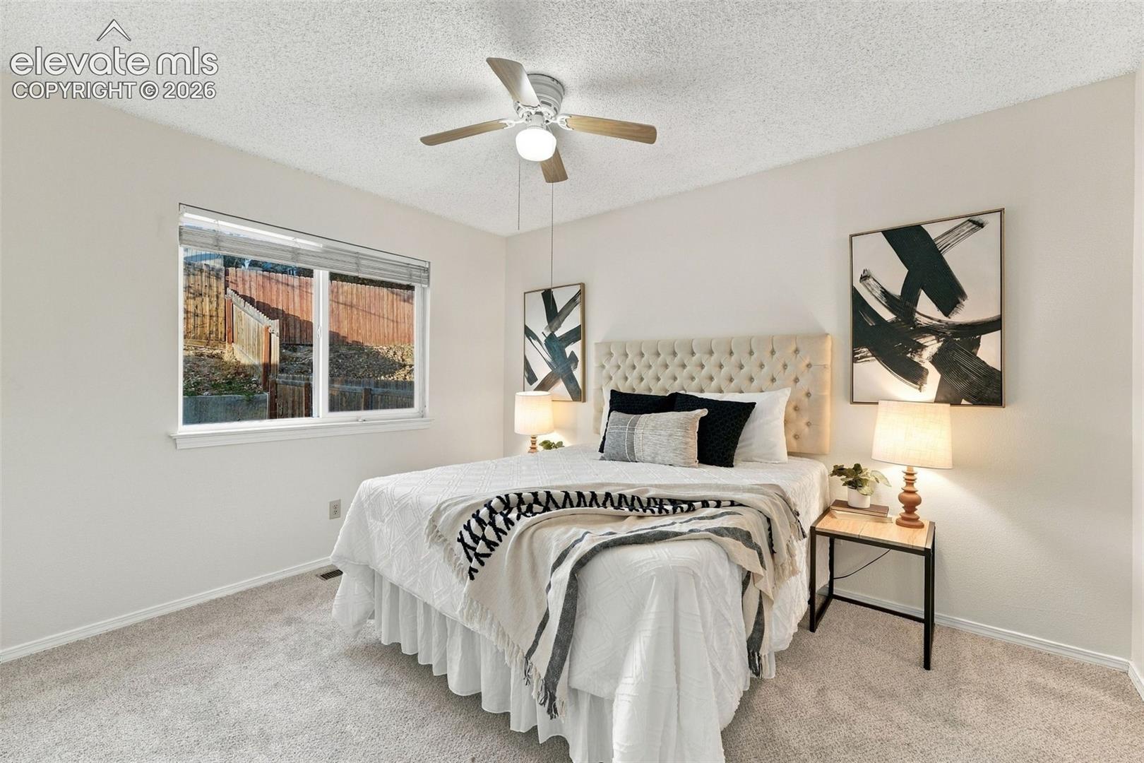 Neutral-toned room with wall-to-wall carpeting, window with blinds, and a ceiling-mounted light fixture with a fan