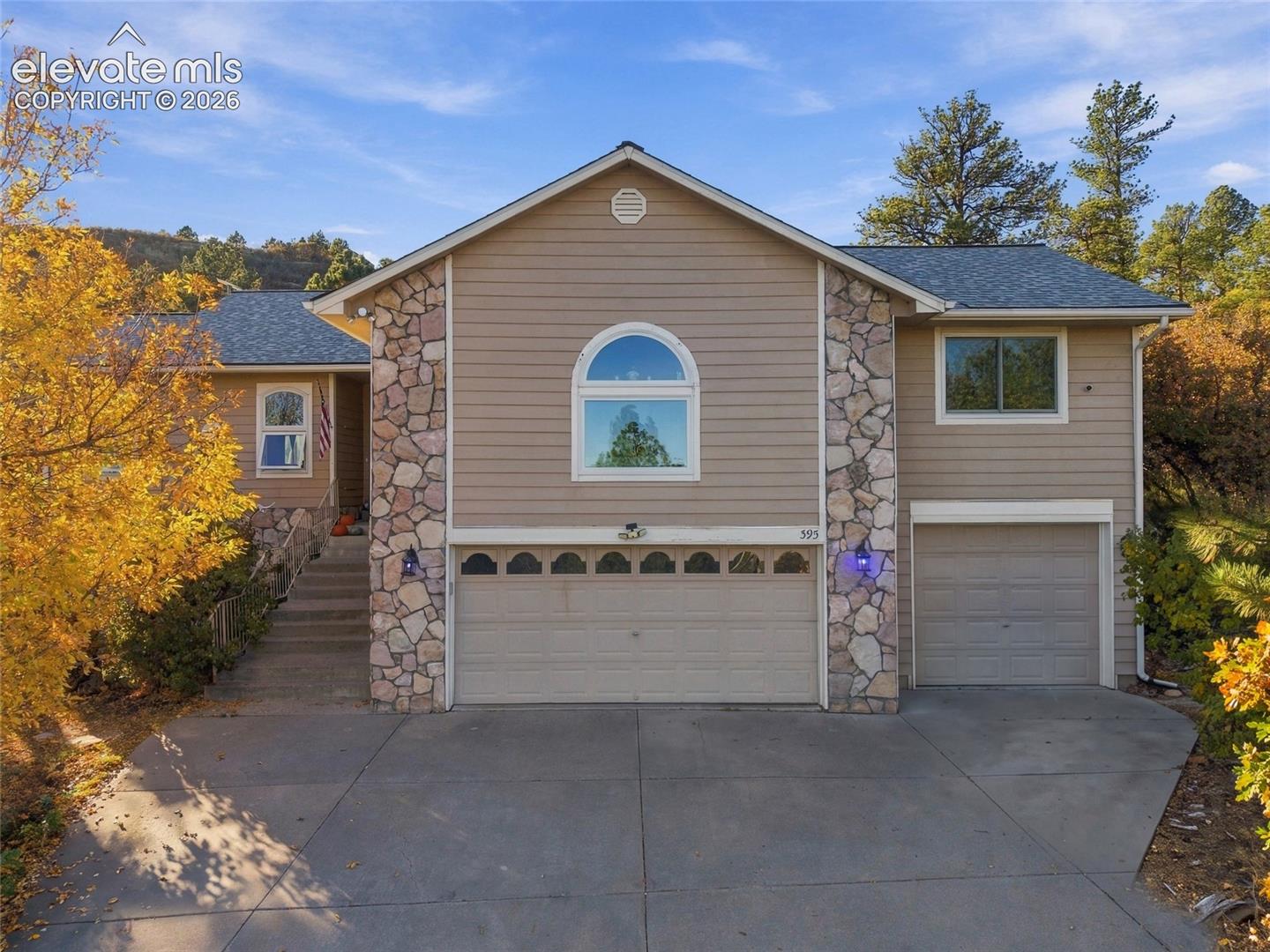 Multi-level exterior featuring horizontal siding, decorative stone masonry accents, a three-car garage, and an arched window