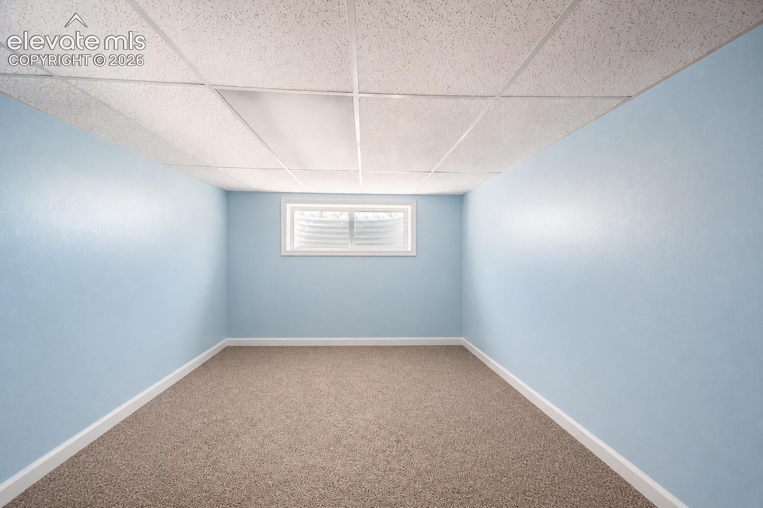 Recessed window with white trim, light blue painted walls, brown carpet flooring, and a dropped ceiling with recessed lighting