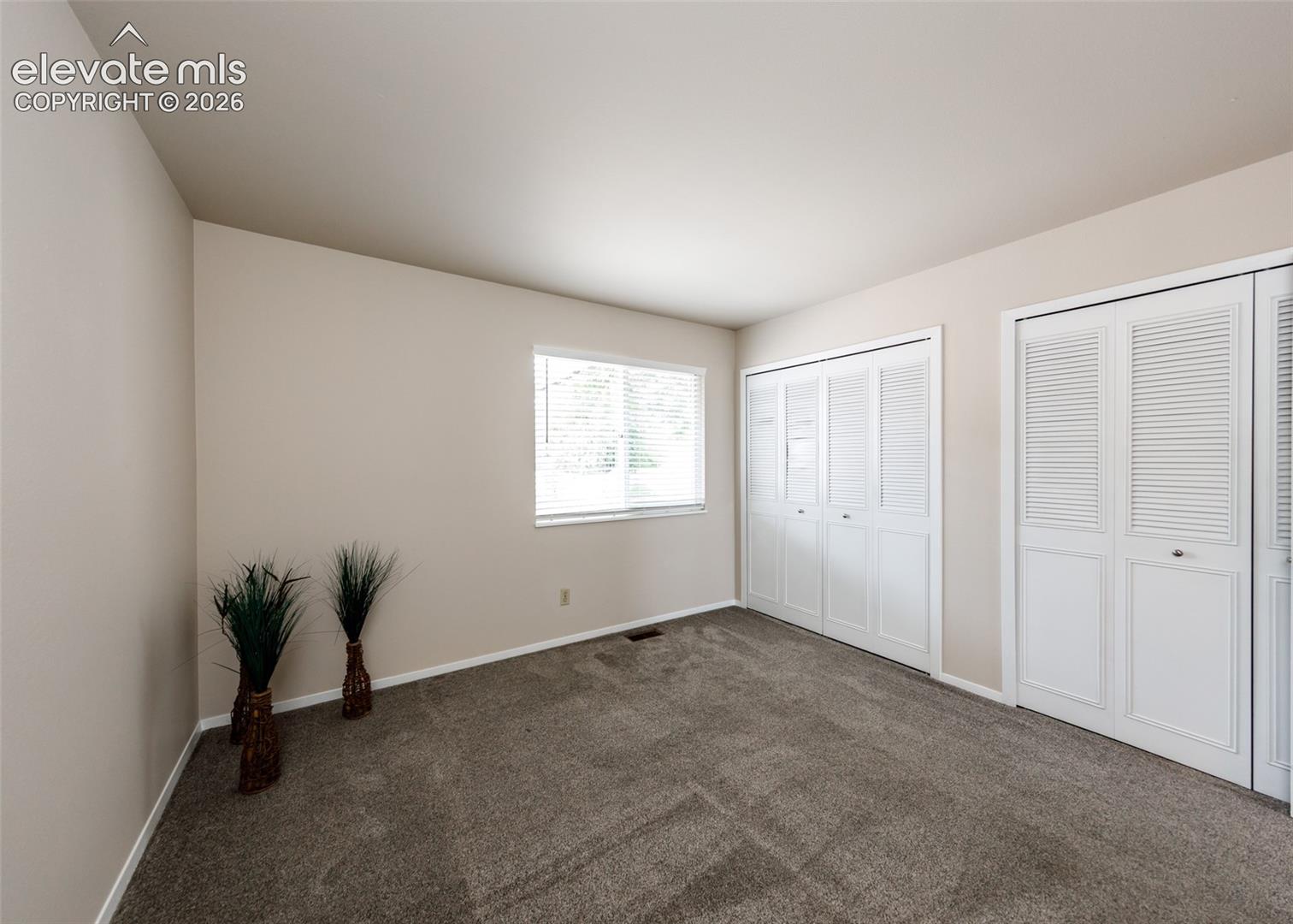 Carpeted room featuring a white-trimmed window with blinds and two sets of louvered bi-fold closet doors
