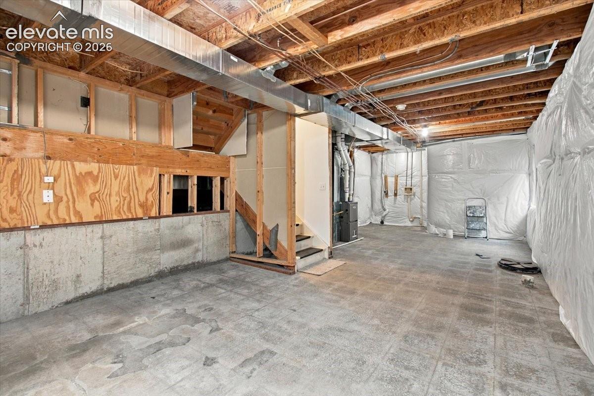 Unfinished lower level featuring exposed wood joist ceilings, concrete foundation walls, plywood paneling, and a floor comprised of square tiles