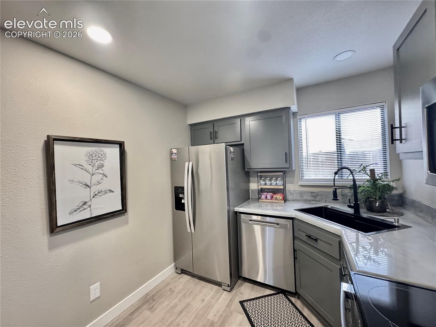 Kitchen featuring shaker-style cabinetry, stainless steel appliances, solid-surface countertops, a matte black faucet, and wood-finish flooring