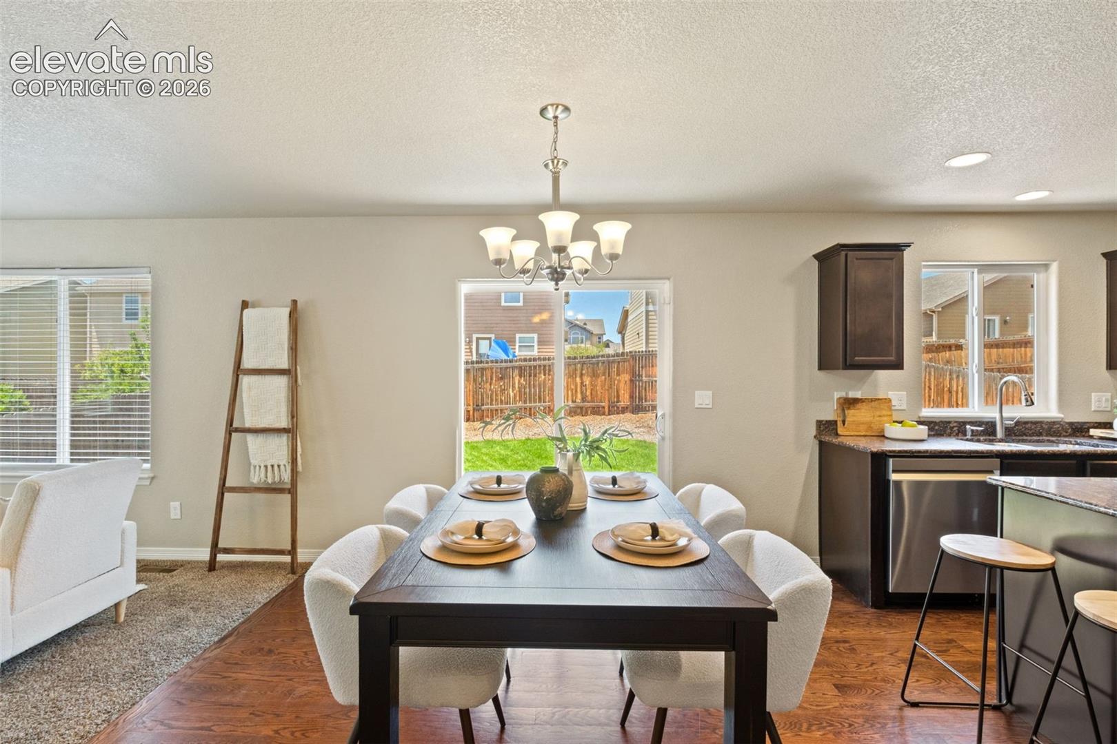 Open-concept living space featuring wood-finish flooring, a contemporary dining area with overhead chandelier, and a sliding glass door leading to a fenced backyard