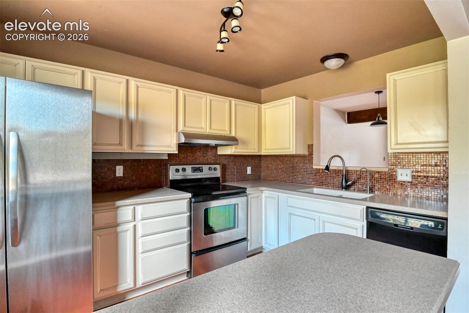 Kitchen featuring stainless steel appliances, light-toned cabinetry, mosaic tile backsplash, and a pass-through window