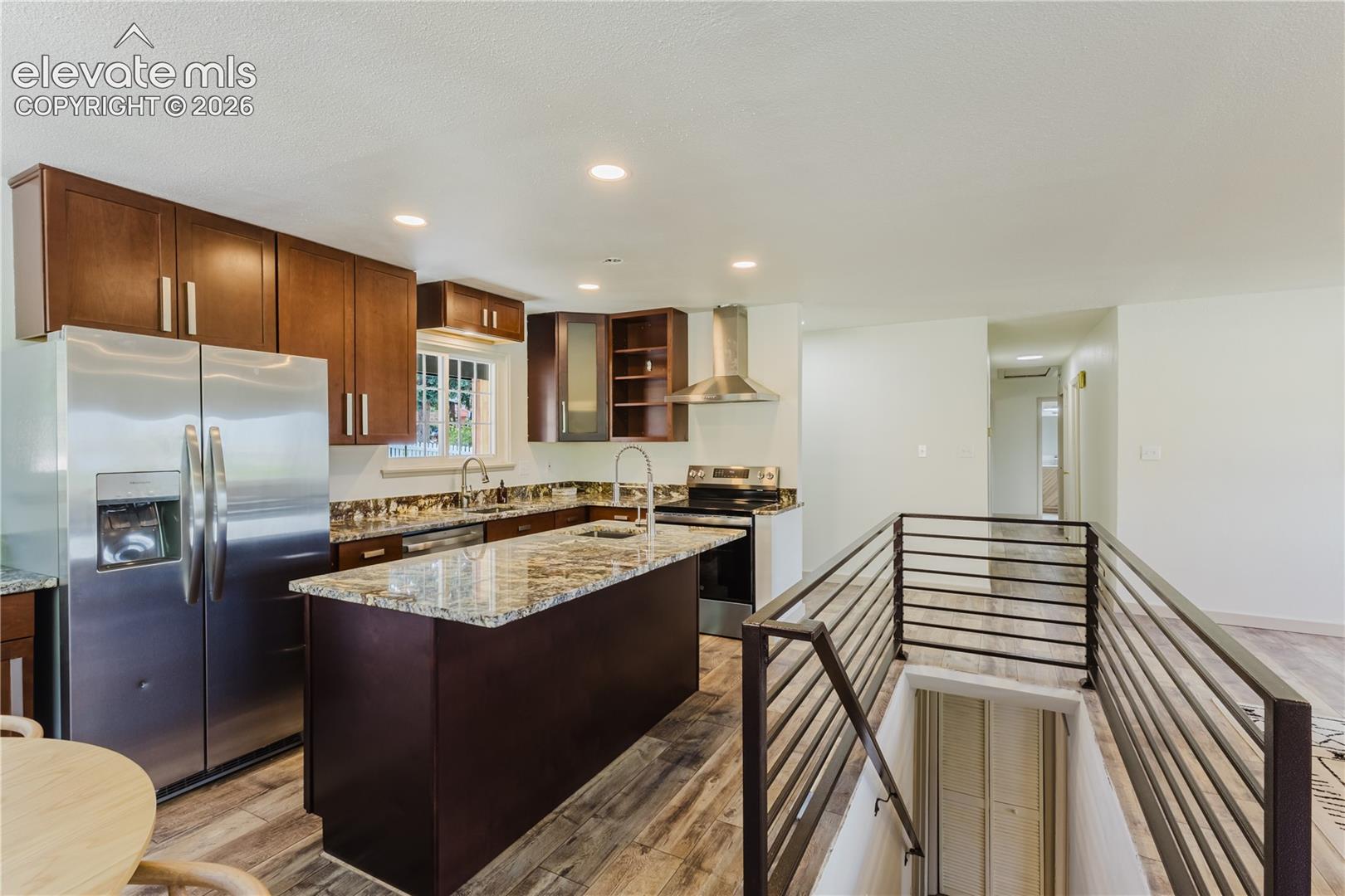Kitchen featuring dark wood cabinetry, stainless steel appliances, a center island with a granite-style countertop, and recessed lighting