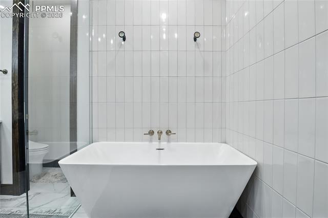 Bathroom with a soaking tub, tile walls, marble finish flooring, and a tile shower