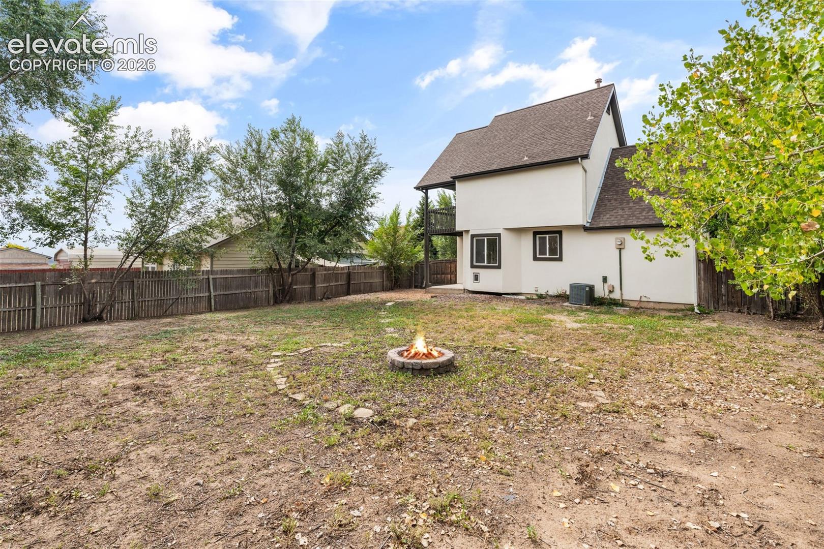 Private backyard featuring a stone-encased fire pit, wood-slat privacy fencing, and an elevated deck