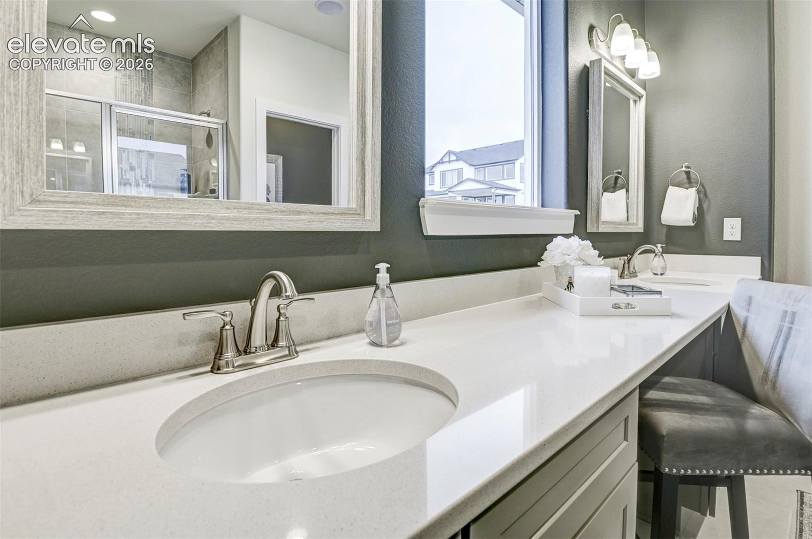 Dual vanity with integrated sinks, brushed nickel fixtures, a framed mirror, and an adjacent shower enclosure with glass doors