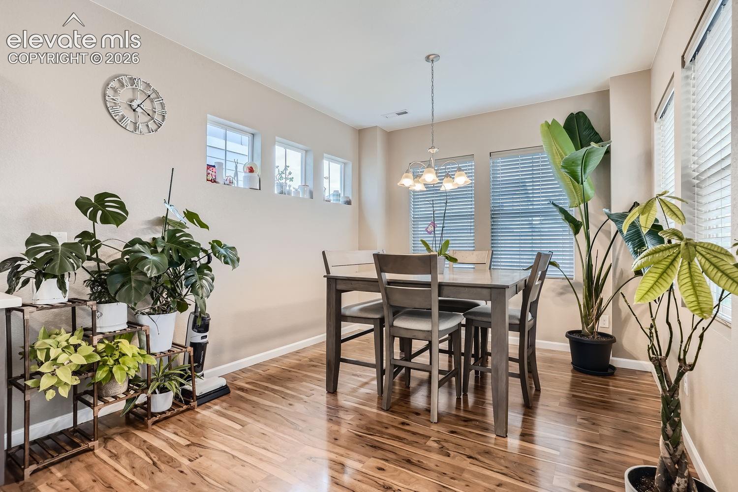 Wood-finish flooring, multi-pane windows with horizontal blinds, built-in wall recessed shelving, and a multi-arm pendant chandelier