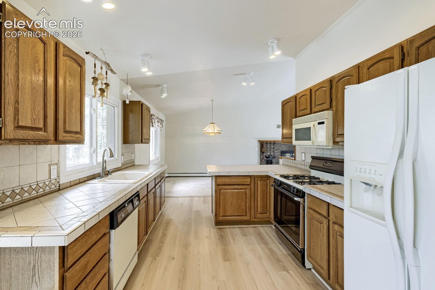 Kitchen featuring wood-finish cabinetry, tile countertops, and a white double sink with a stainless steel faucet