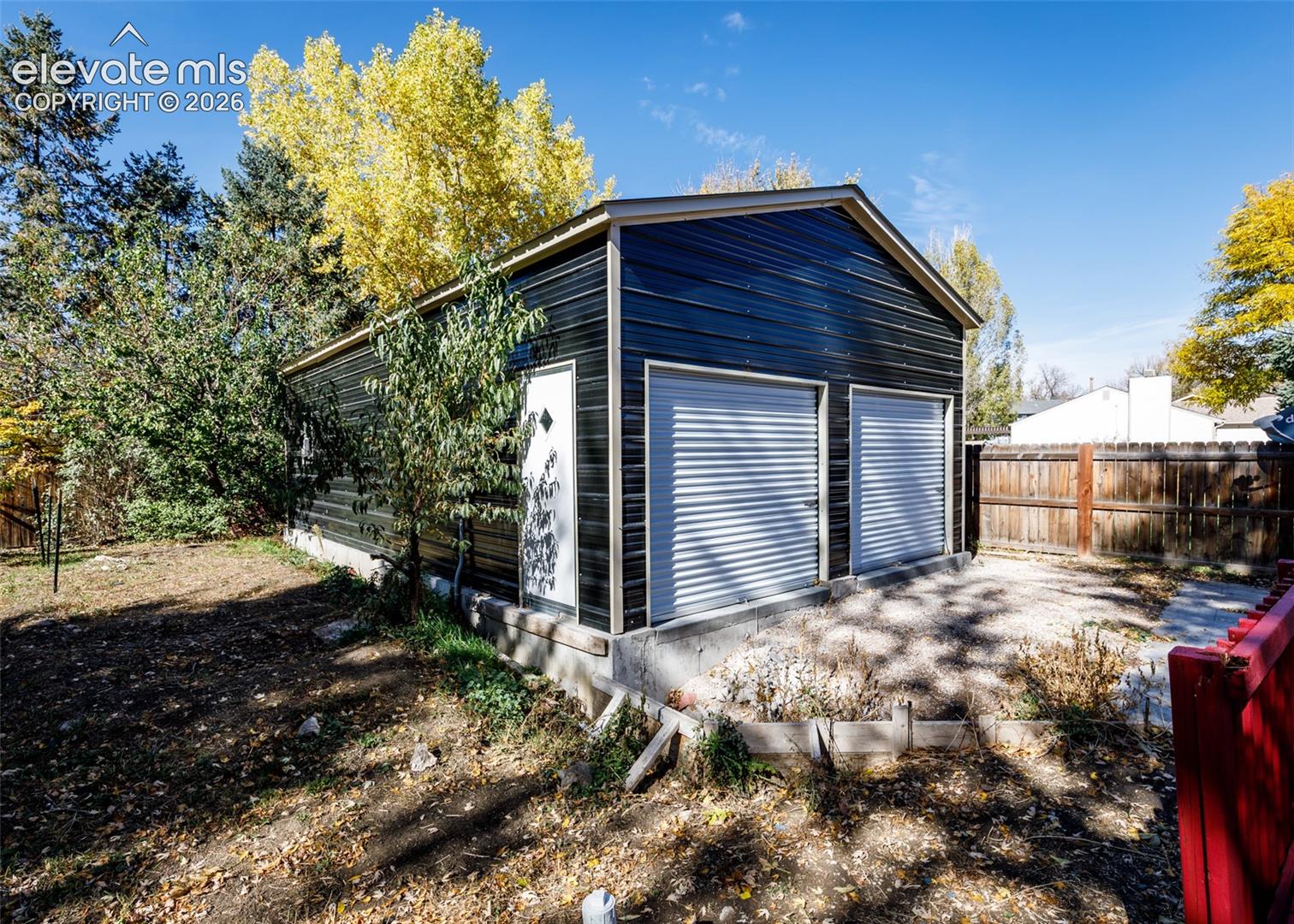 Detached two-car garage featuring dark metal siding, dual roll-up doors, a side-entry pedestrian door, and a concrete foundation
