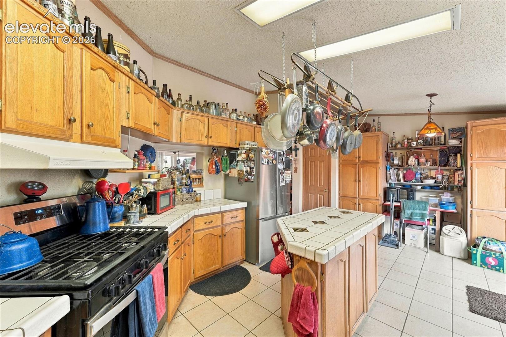 Kitchen featuring wood cabinetry, tiled countertops, a center island with a tiled surface, overhead pot rack, and ceramic tile flooring
