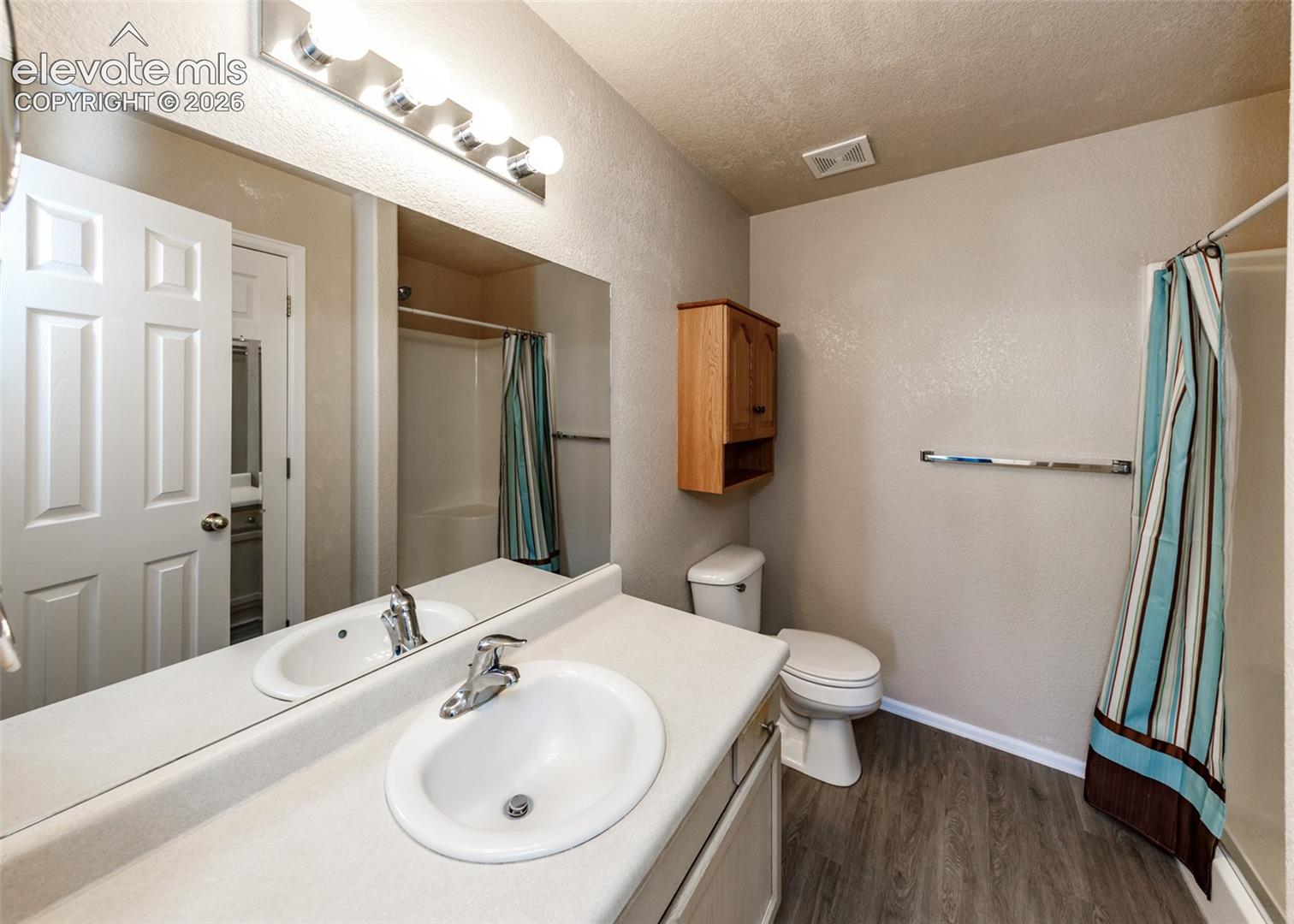 Vanity with a solid surface countertop and integrated oval sink, full-width mirror, wall-mounted wood cabinetry, and wood-finish flooring