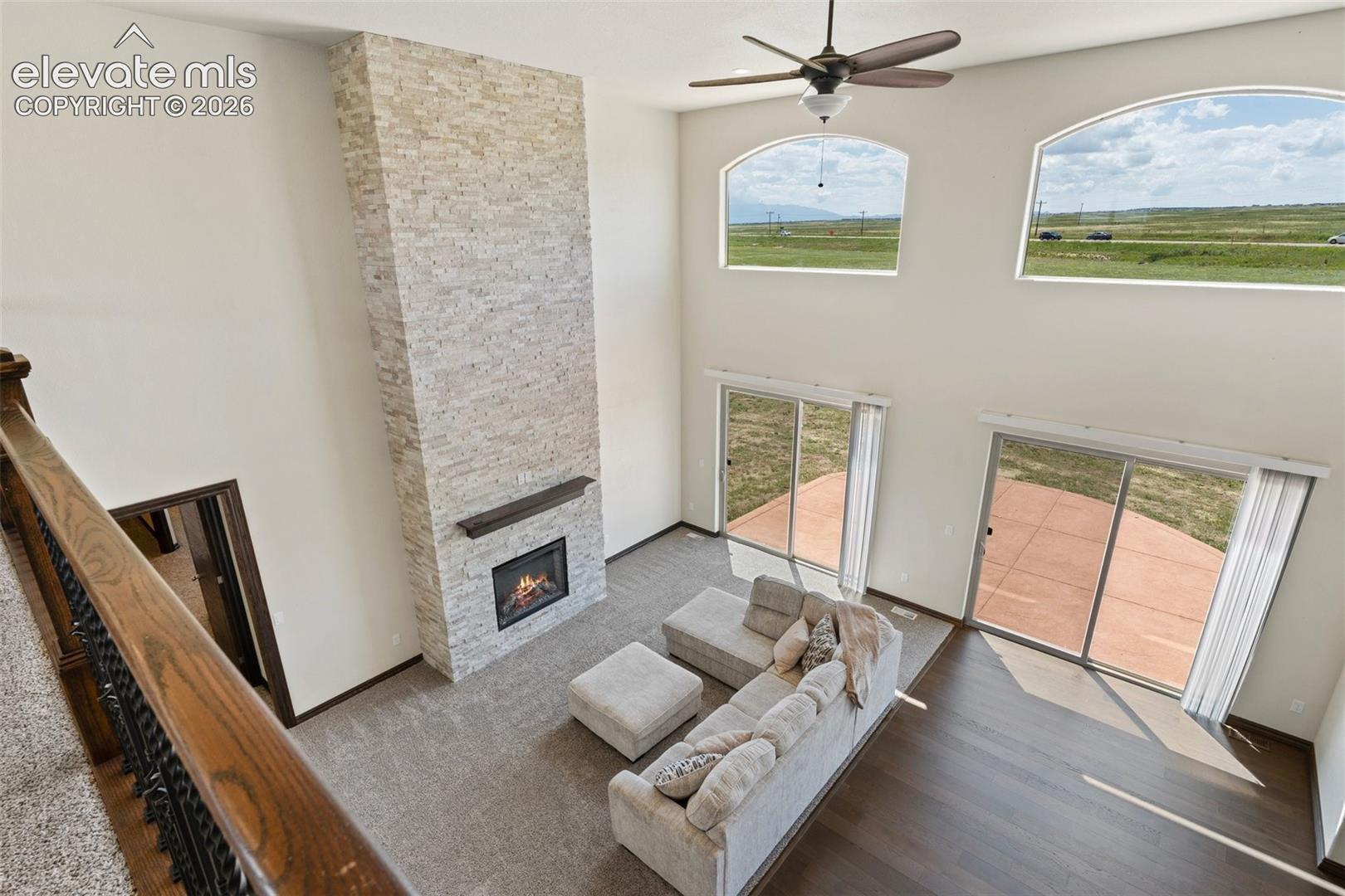 Two-story living area featuring a stacked stone fireplace with wood mantel, arched upper windows, and dual sliding glass doors