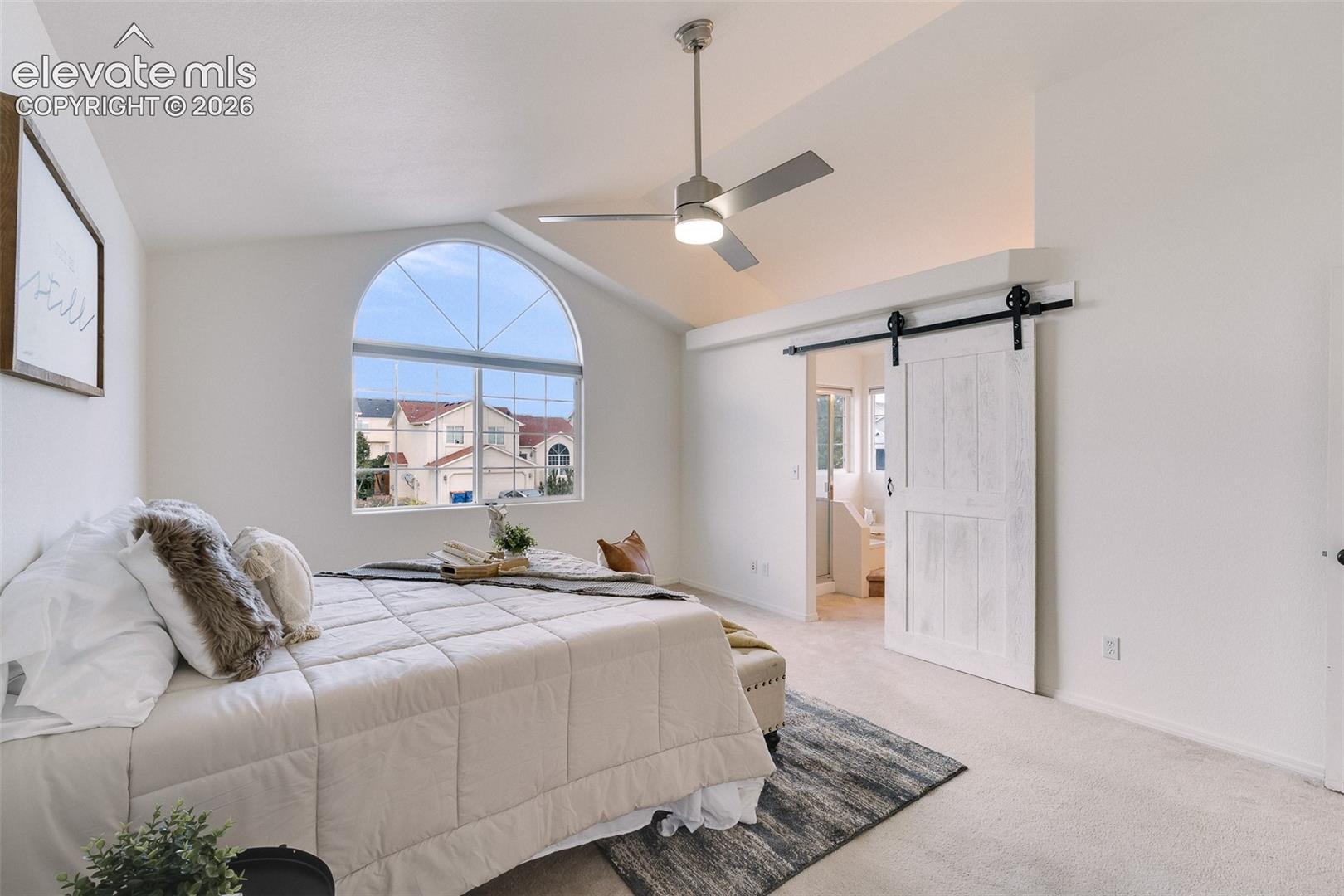 Vaulted ceiling, arched window, ceiling fan, carpet flooring, and barn door entry