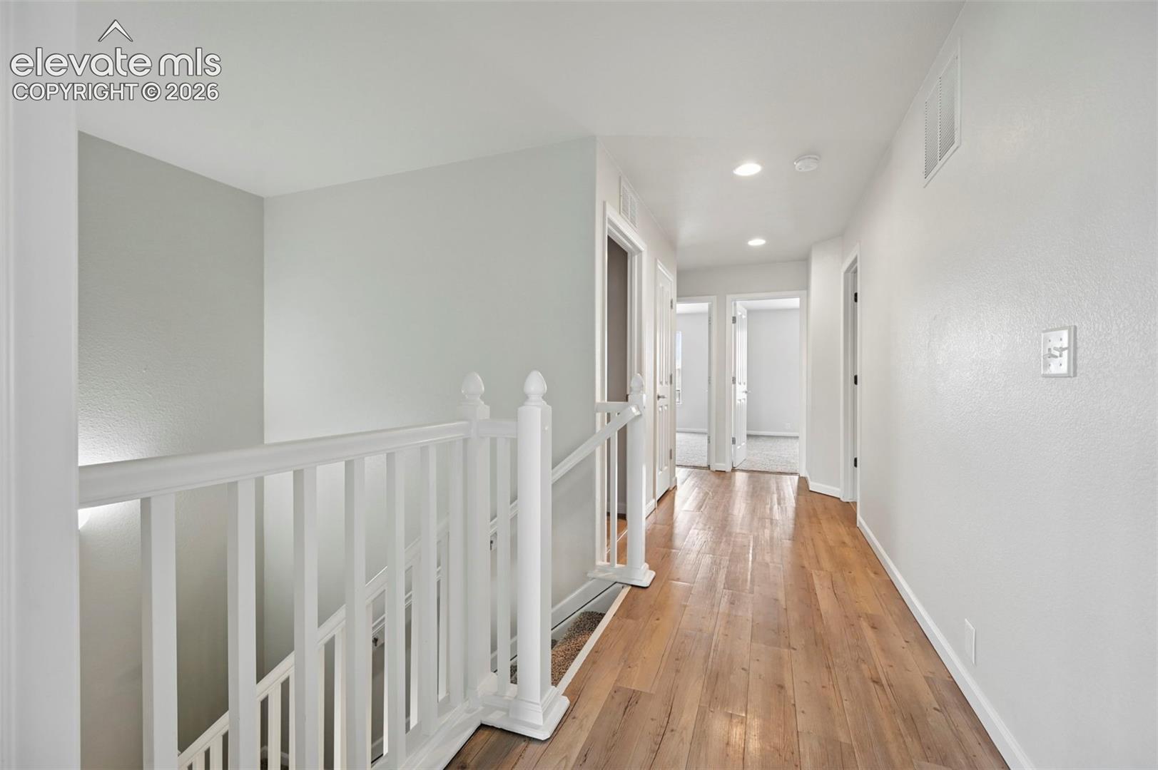 Upper-level hallway featuring wood-finish flooring, white walls, recessed lighting, and multiple doorways