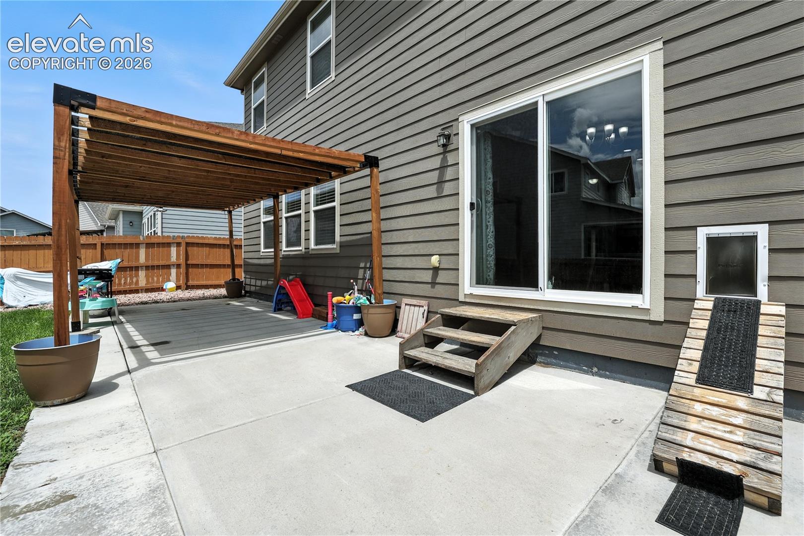 Concrete patio featuring a wood pergola, vinyl siding, sliding glass door, and a pet door with ramp