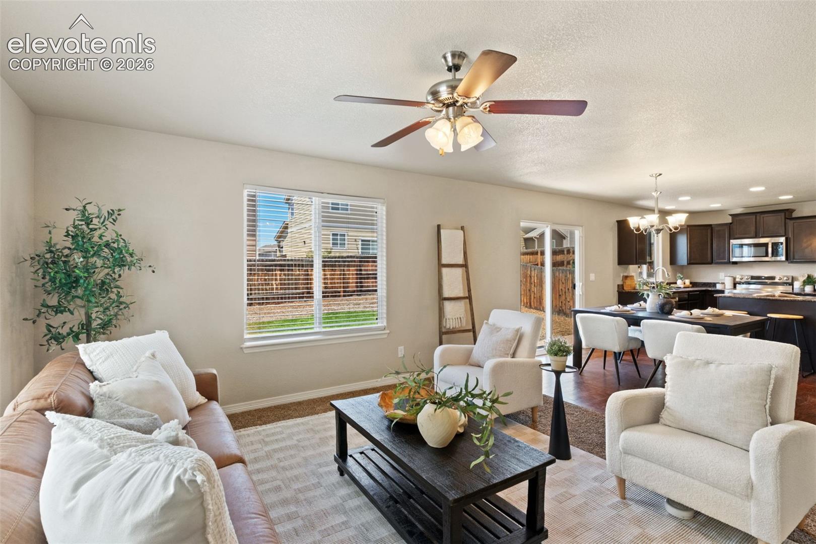 Open-concept living space featuring a ceiling fan with integrated lighting, a large window with blinds, and wood-finish flooring