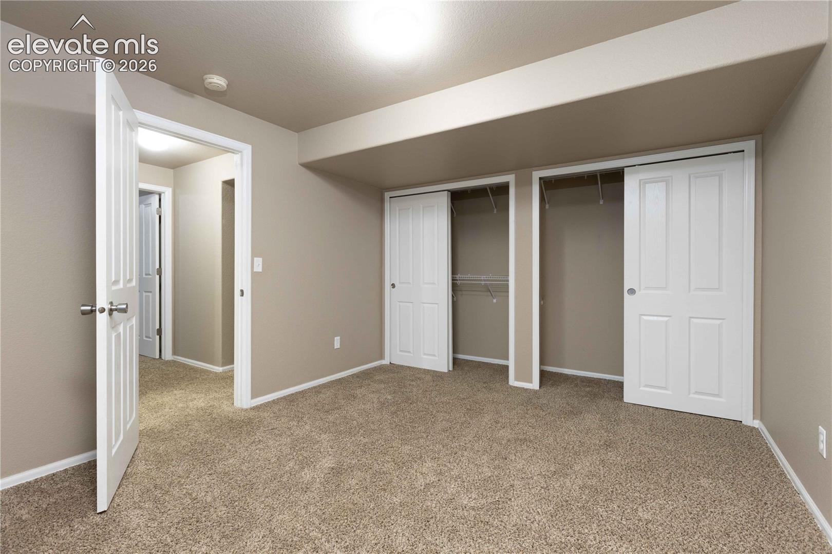 Neutral-toned interior featuring wall-to-wall carpeting, dual closets with white paneled doors, and a ceiling-mounted light fixture