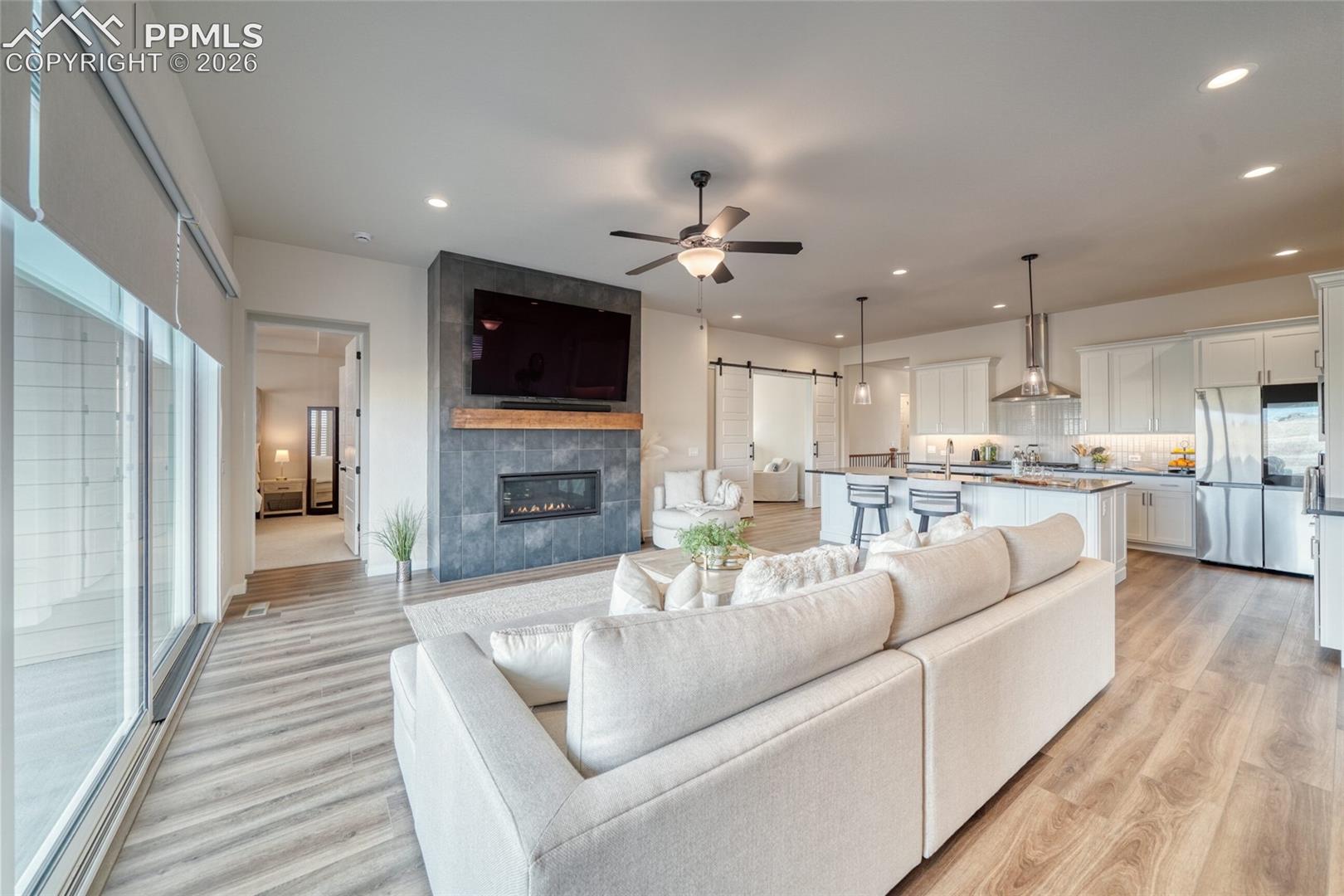 Living area with a barn door, ceiling fan, a tile fireplace, light wood-style floors, and recessed lighting
