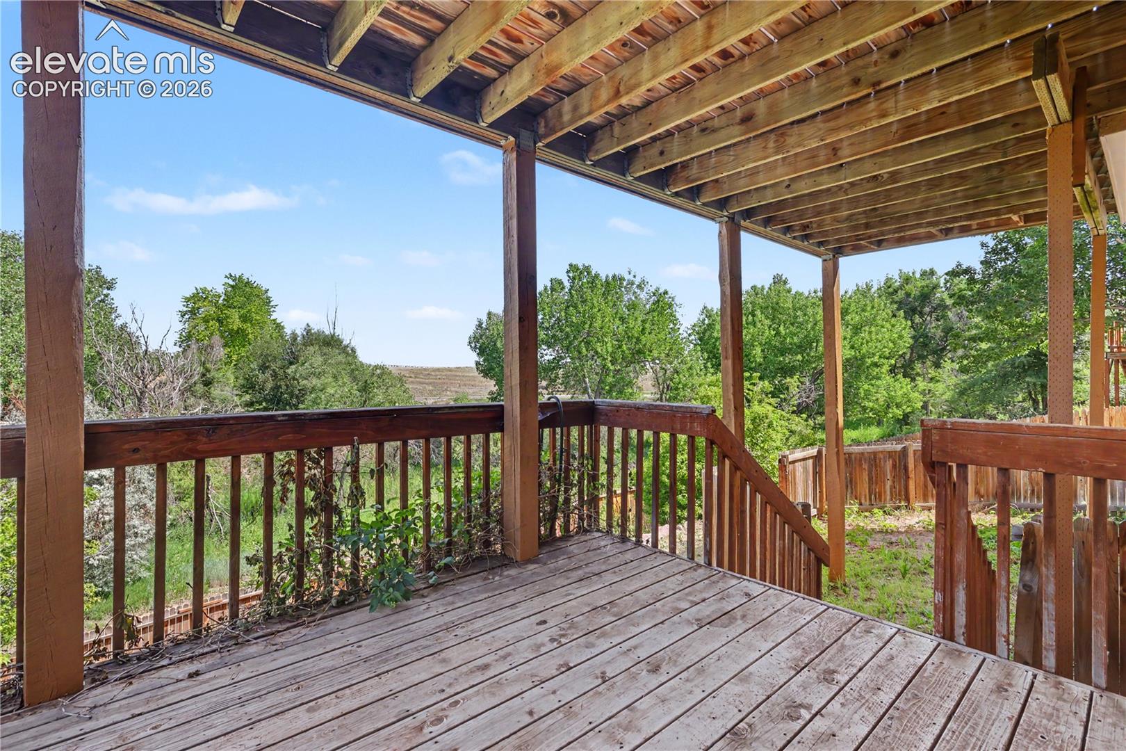 Spacious wood-finish deck featuring a full railing system, exposed wood joists, and open-air design overlooking natural landscaping.