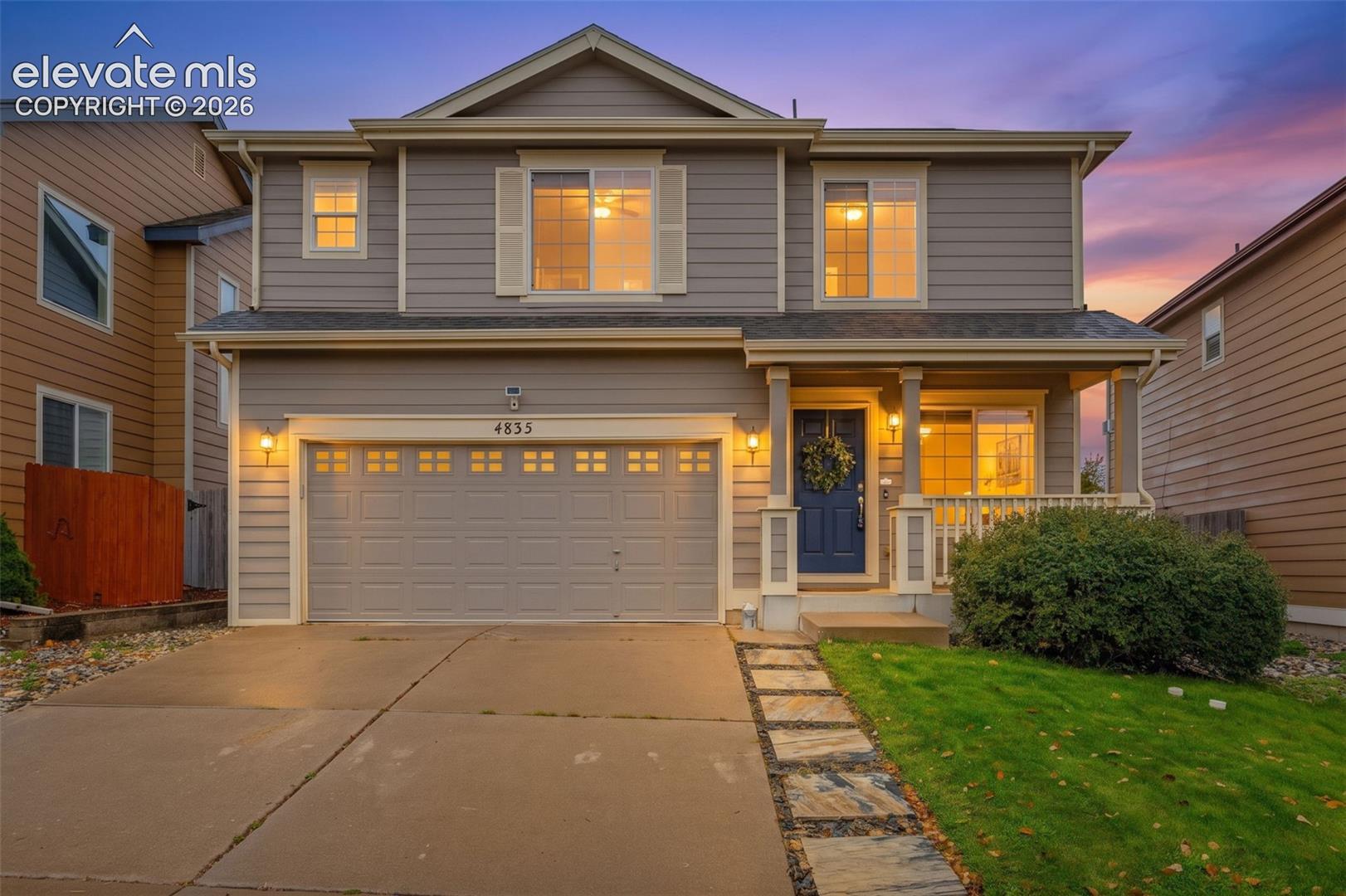 Two-story residence featuring horizontal lap siding, a two-car garage with paneled door, a covered front porch with column supports, and a stone-paver walkway