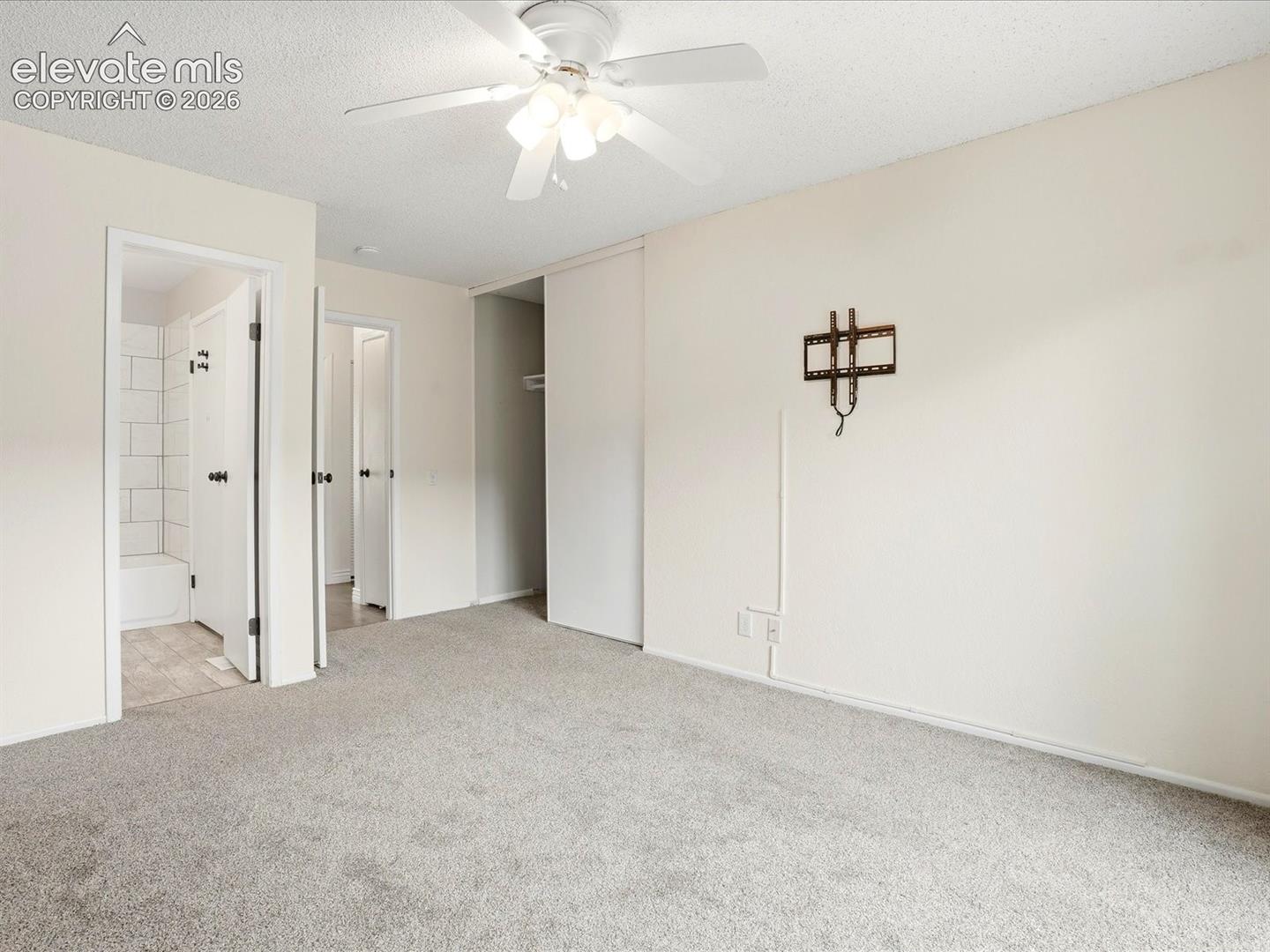 Neutral-toned room featuring neutral carpeting, a ceiling fan with integrated lighting, and sliding-panel closet doors