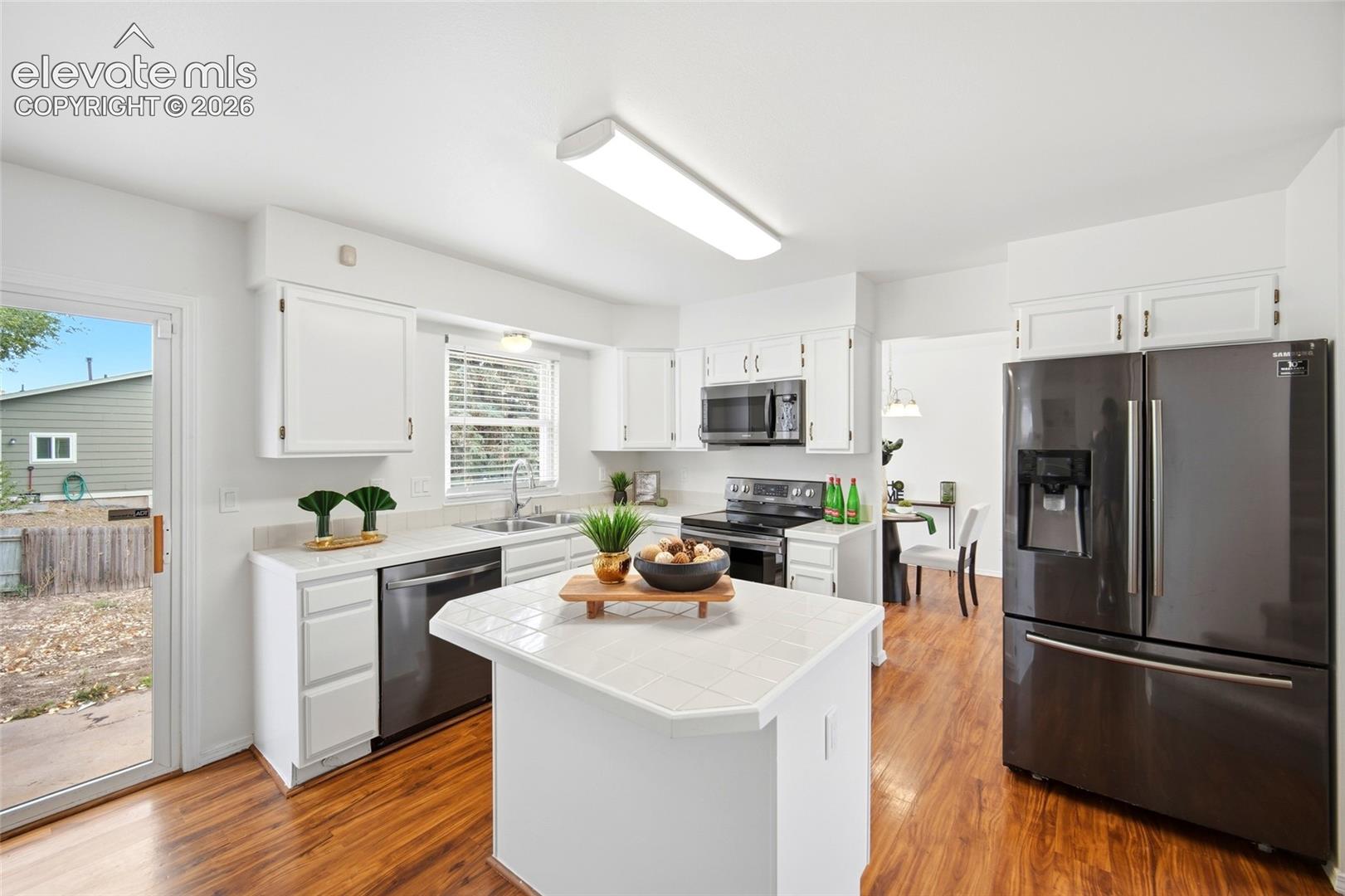 Kitchen featuring white cabinetry, tile-topped center island, wood-finish flooring, dark-finish appliances, and glass-paned door