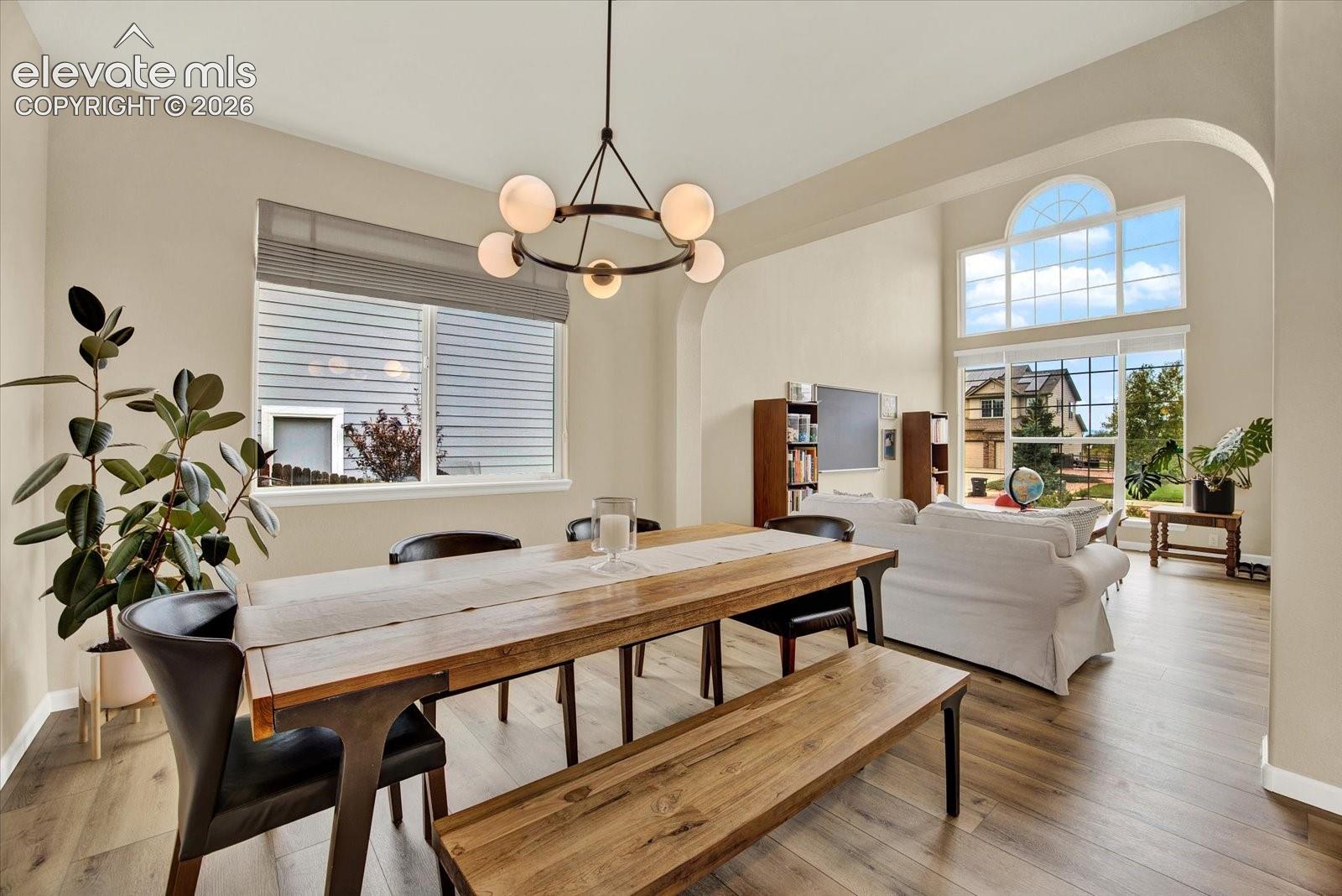 Open-concept interior featuring high ceilings, wood-finish flooring, multi-light orb chandelier, arched architectural detailing, and large windows with arched transom top