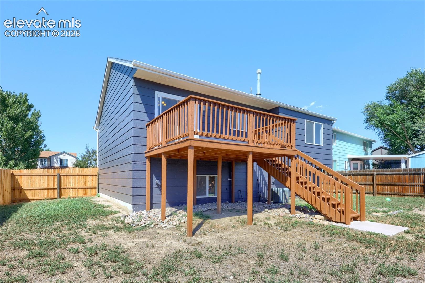Rear exterior featuring a wood deck, wood staircase, horizontal siding, and a wood fence