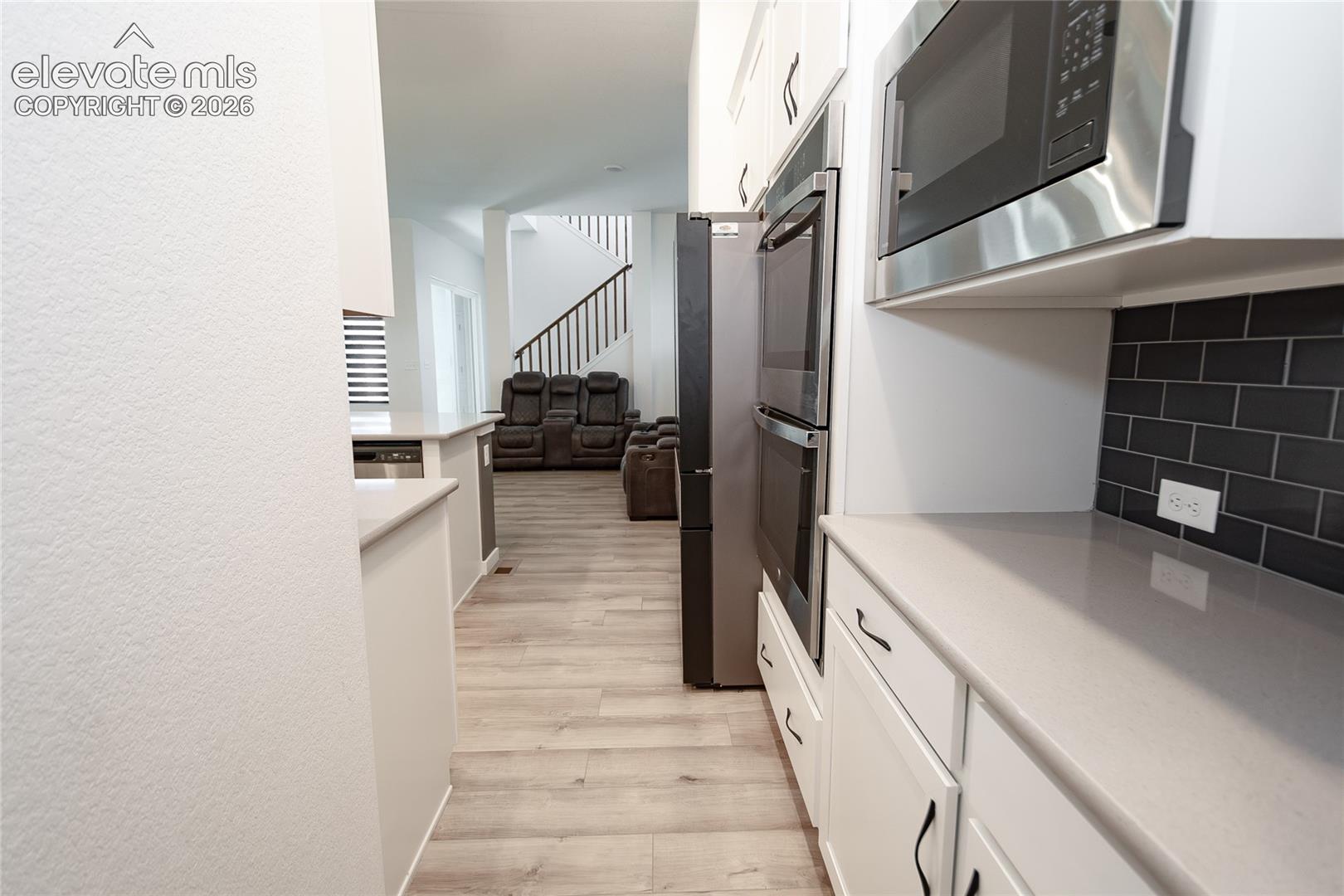 Kitchen featuring white shaker-style cabinetry, solid-surface countertops, dark subway tile backsplash, and stainless-steel built-in wall oven and microwave