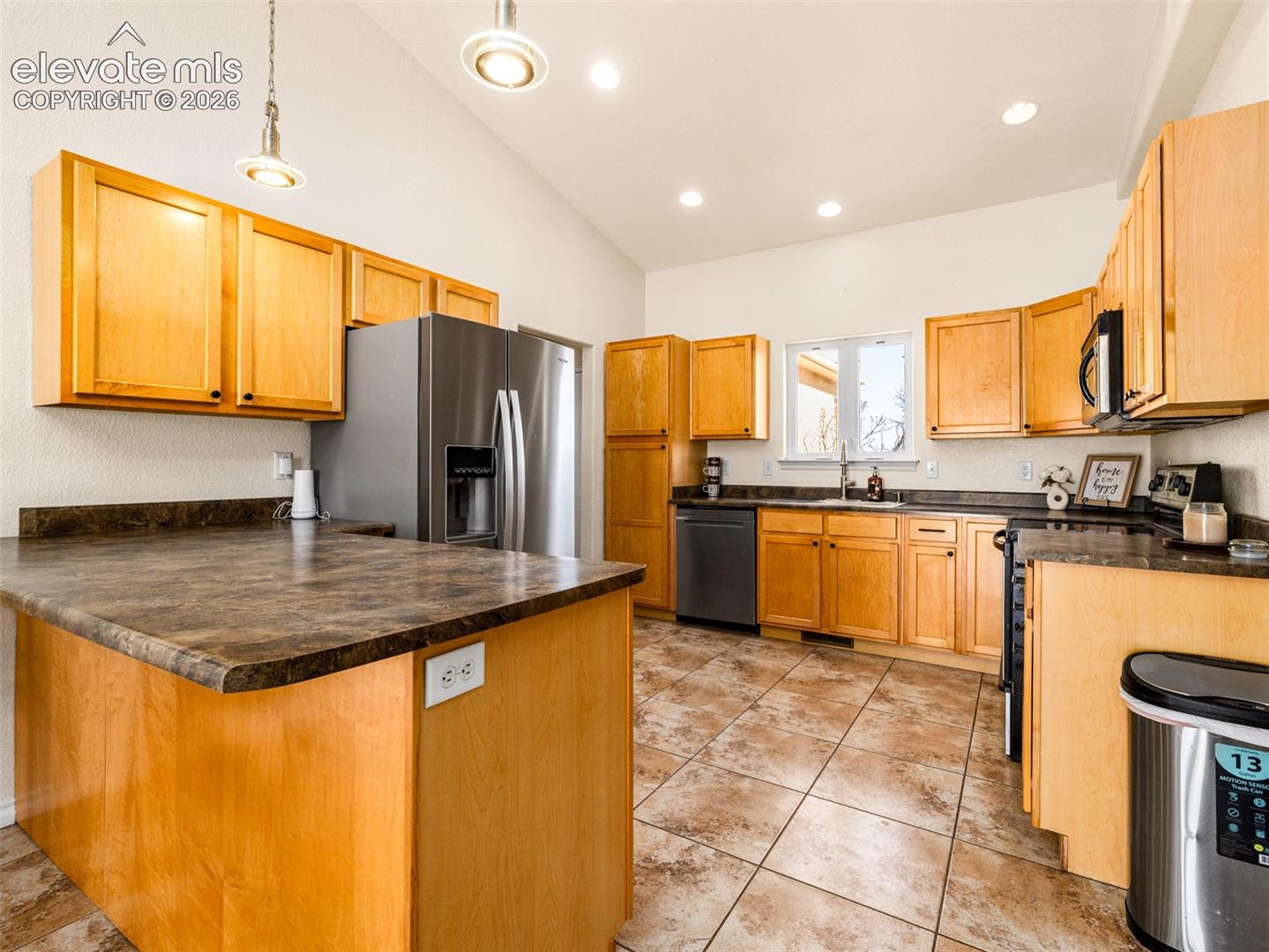 Vaulted ceiling with recessed lighting, stainless steel appliances, wood-finish cabinetry, tile flooring, and a kitchen island with seating