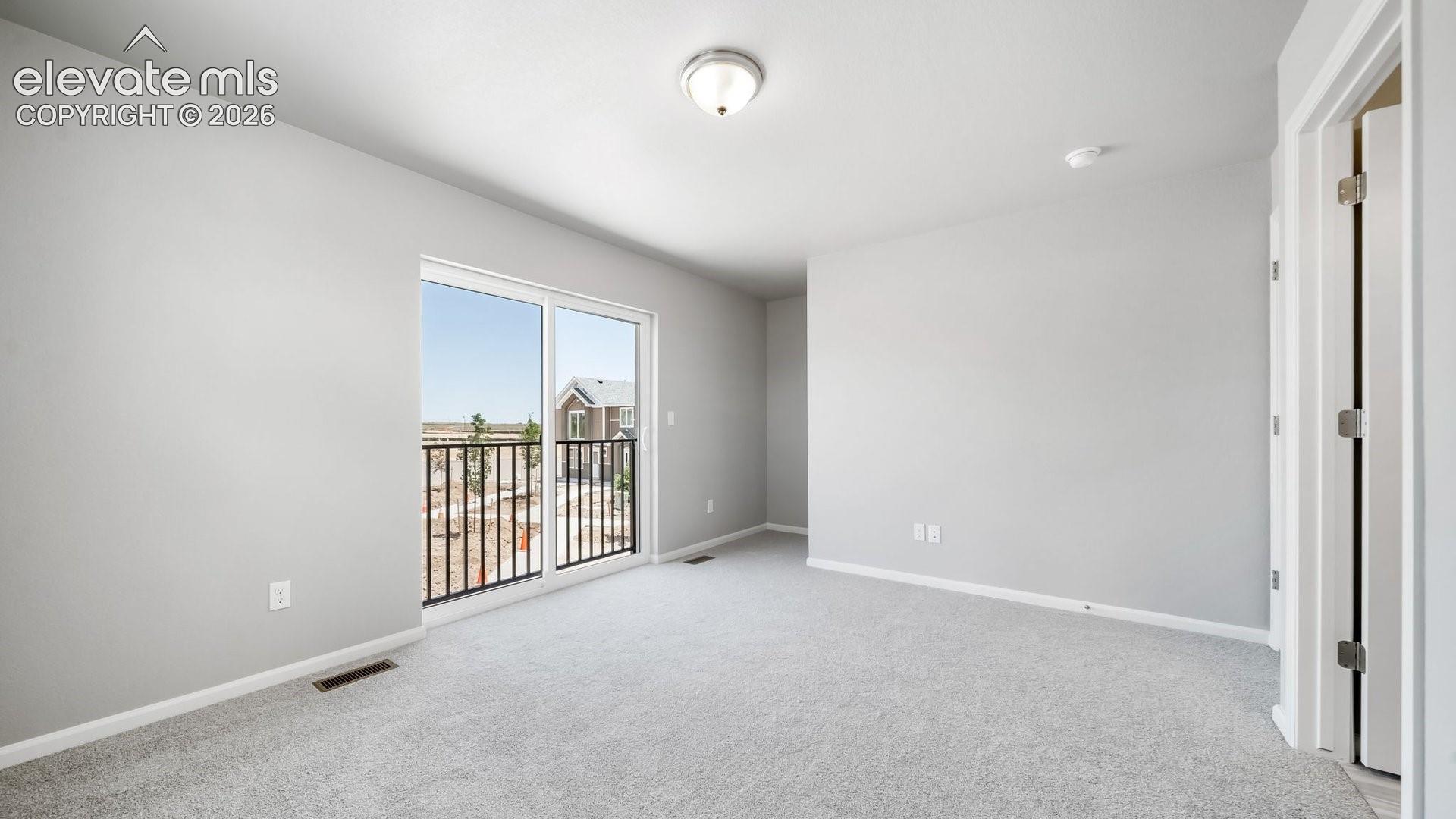 Neutral-toned interior space featuring light grey wall paint, plush carpeting, a glass sliding door, and a metal-railed exterior balcony
*photos of a model home*