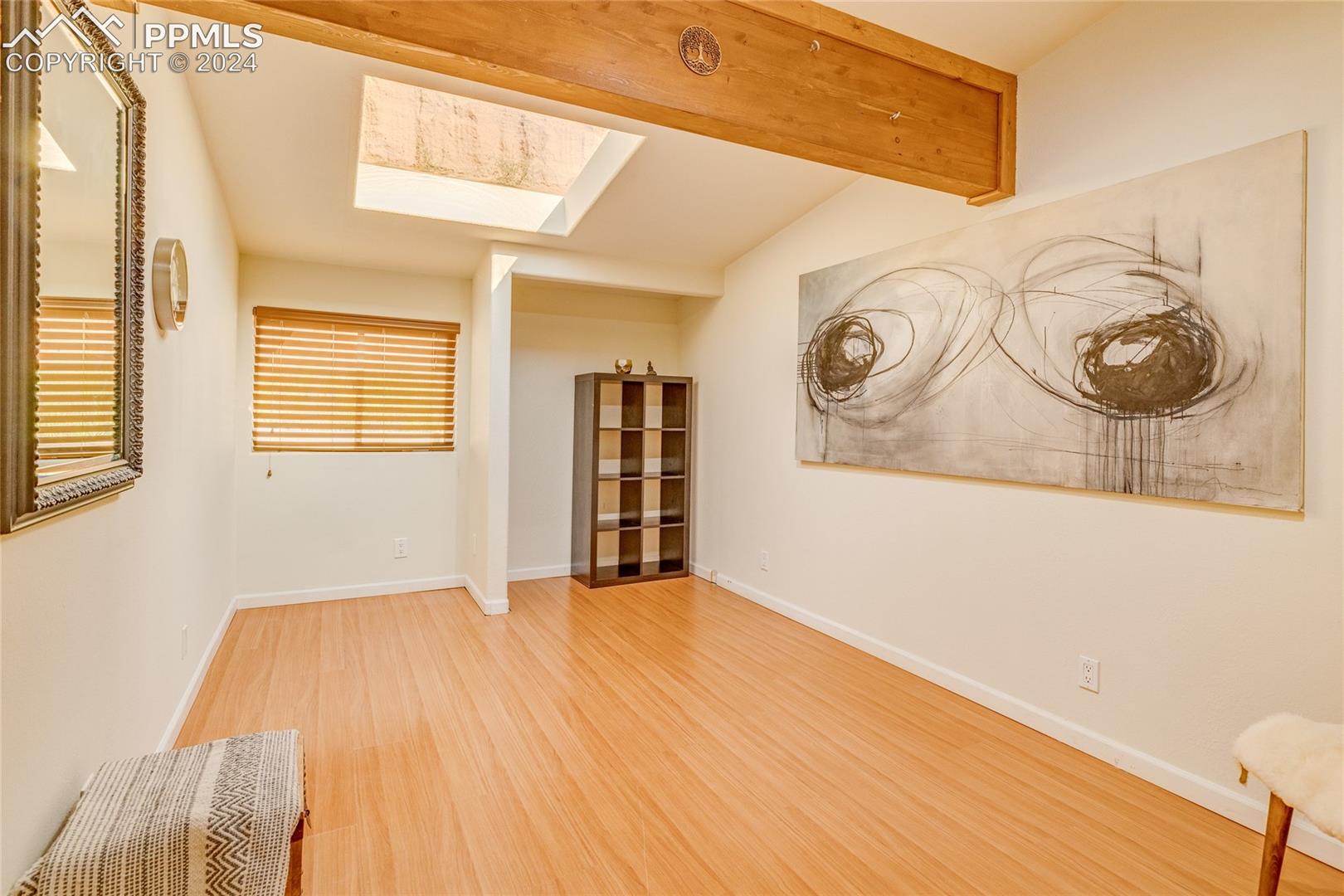 Empty room featuring vaulted ceiling with skylight and light wood-type flooring