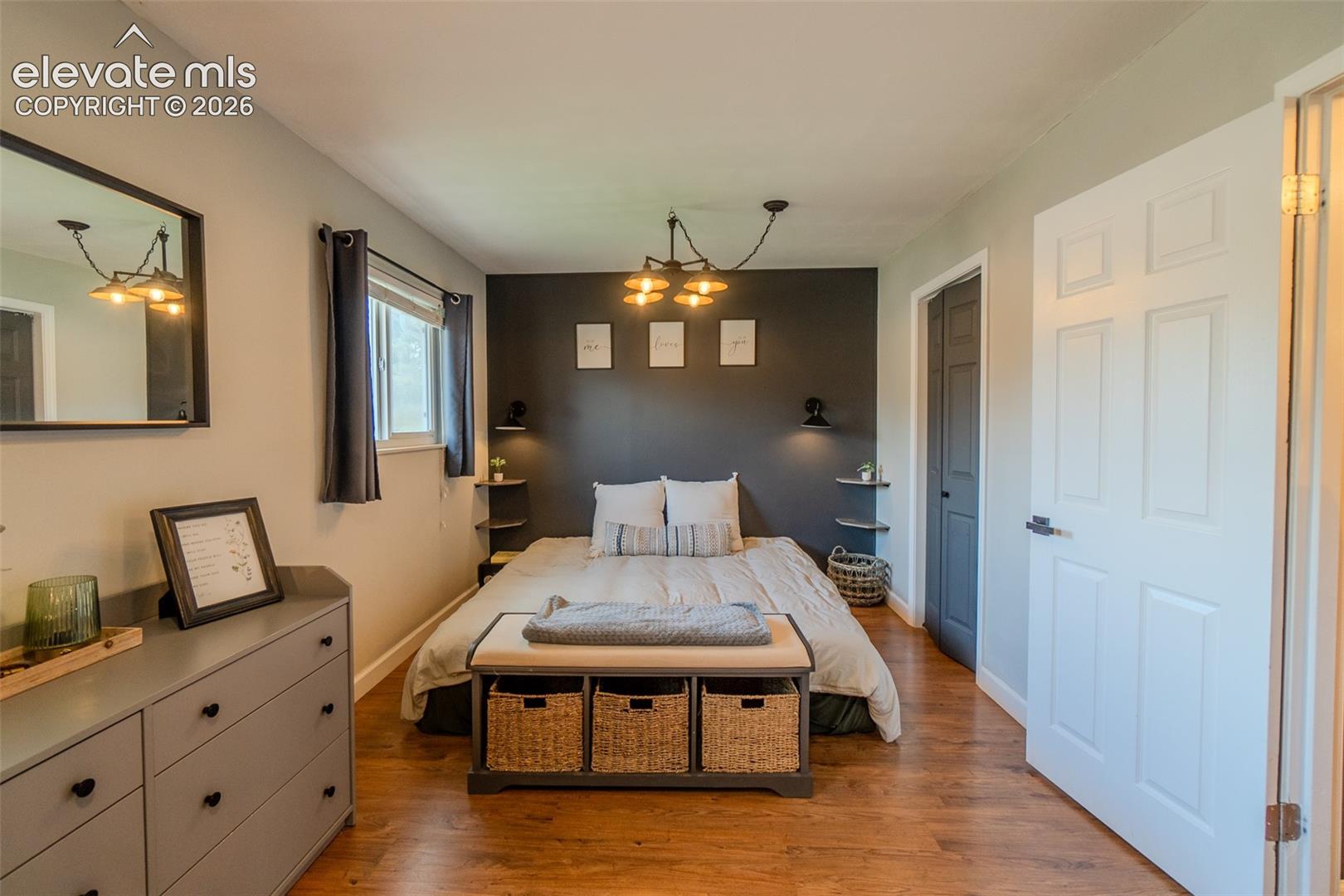 Room featuring wood-finish flooring, a dark charcoal accent wall, integrated wall-mounted shelving, six-panel interior doors, and a multi-arm industrial-style ceiling fixture