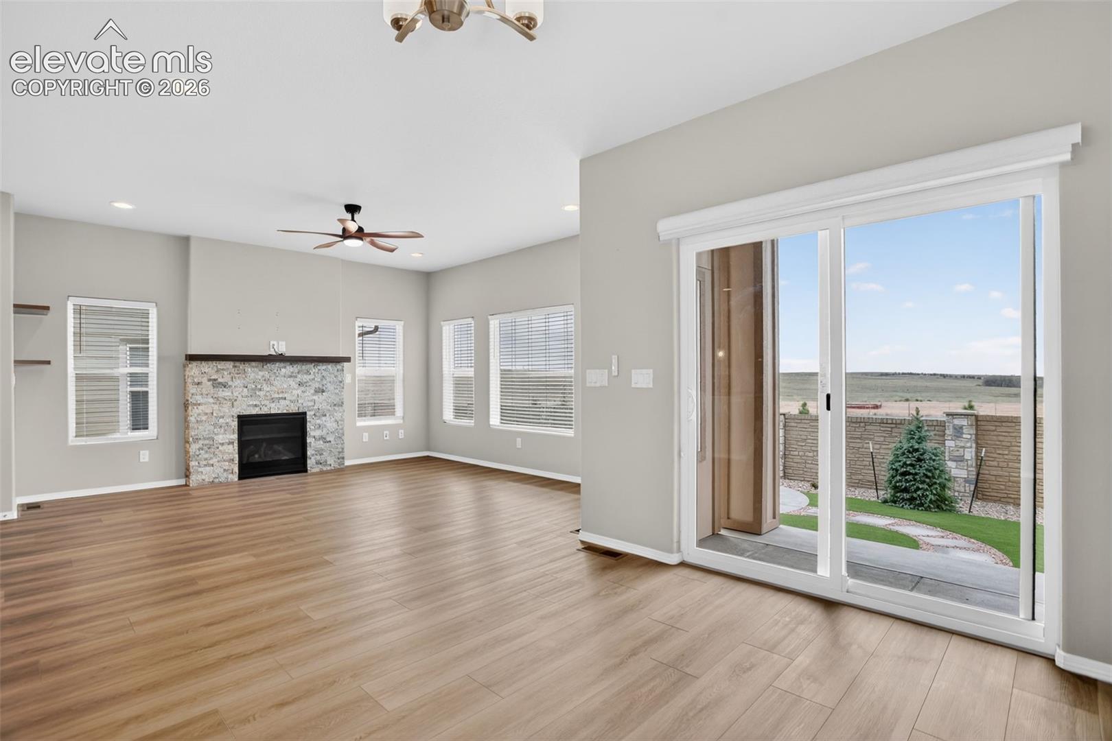 Spacious living area featuring wood-finish flooring, a stone-clad fireplace with a dark mantel, and recessed ceiling lights