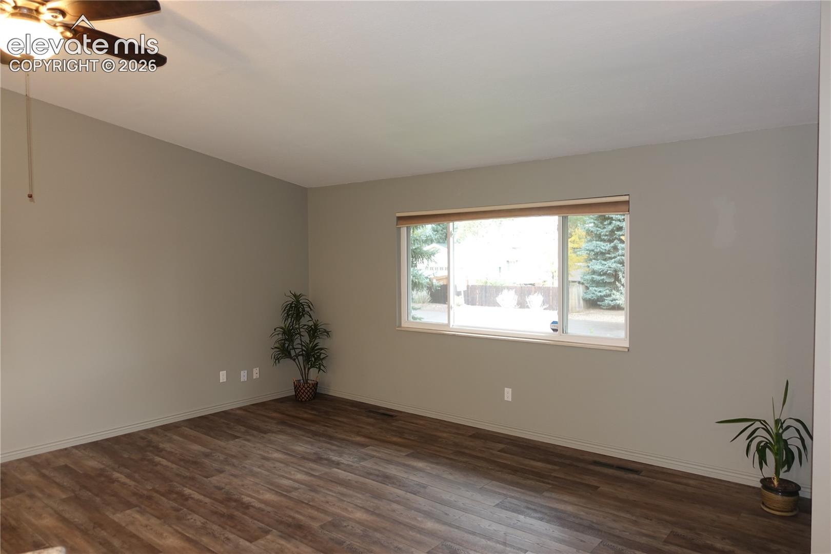 Living area featuring wood-finish flooring, neutral wall paint, and a sliding window with a horizontal blind, finished with an overhead ceiling fan