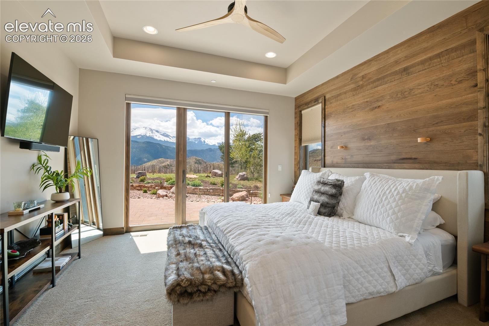 Where guests get the royal treatment. Sophisticated upper-level junior suite featuring an architectural ceiling detail, statement wood-clad accent wall, sliding glass doors to the backyard, and direct Pikes Peak views.