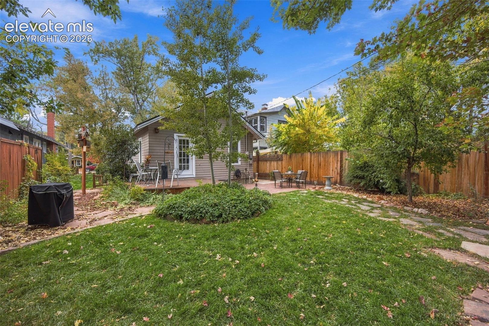 Private backyard featuring a flagstone patio, manicured lawn, perimeter wood fencing, and mature trees