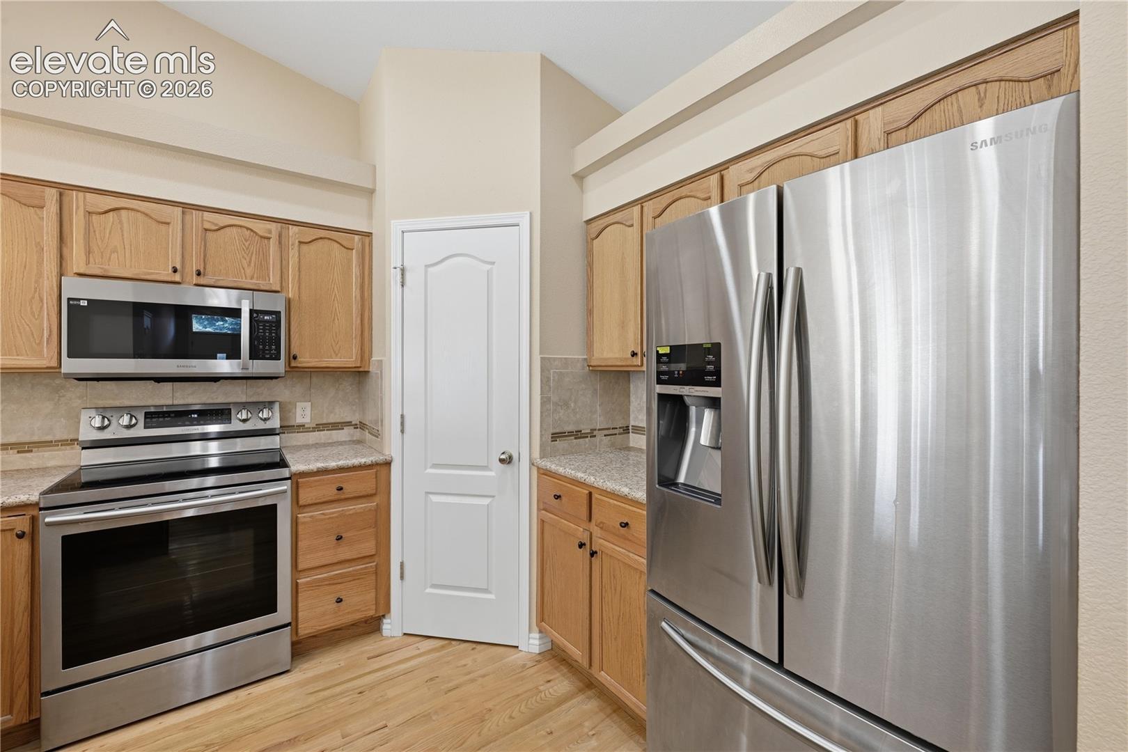 Kitchen featuring light wood cabinetry, stone-finish countertops, stainless steel appliances, and wood-finish flooring