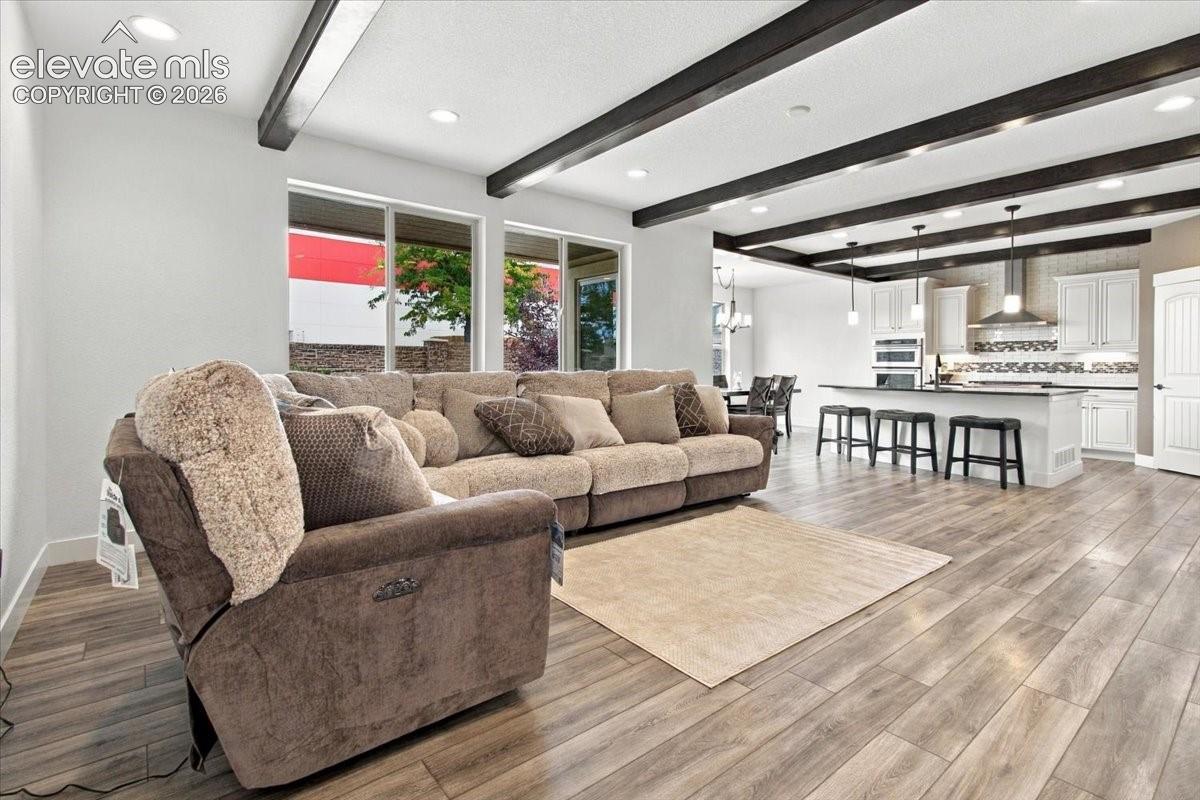 Open floor plan featuring wood-finish flooring, exposed ceiling beams, recessed lighting, and a kitchen equipped with white cabinetry, a center island, and stainless steel appliances