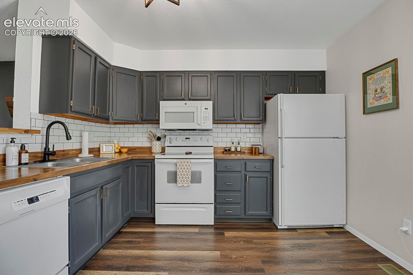 Kitchen with wood-finish flooring, white subway tile backsplash, dark cabinetry, and white appliances