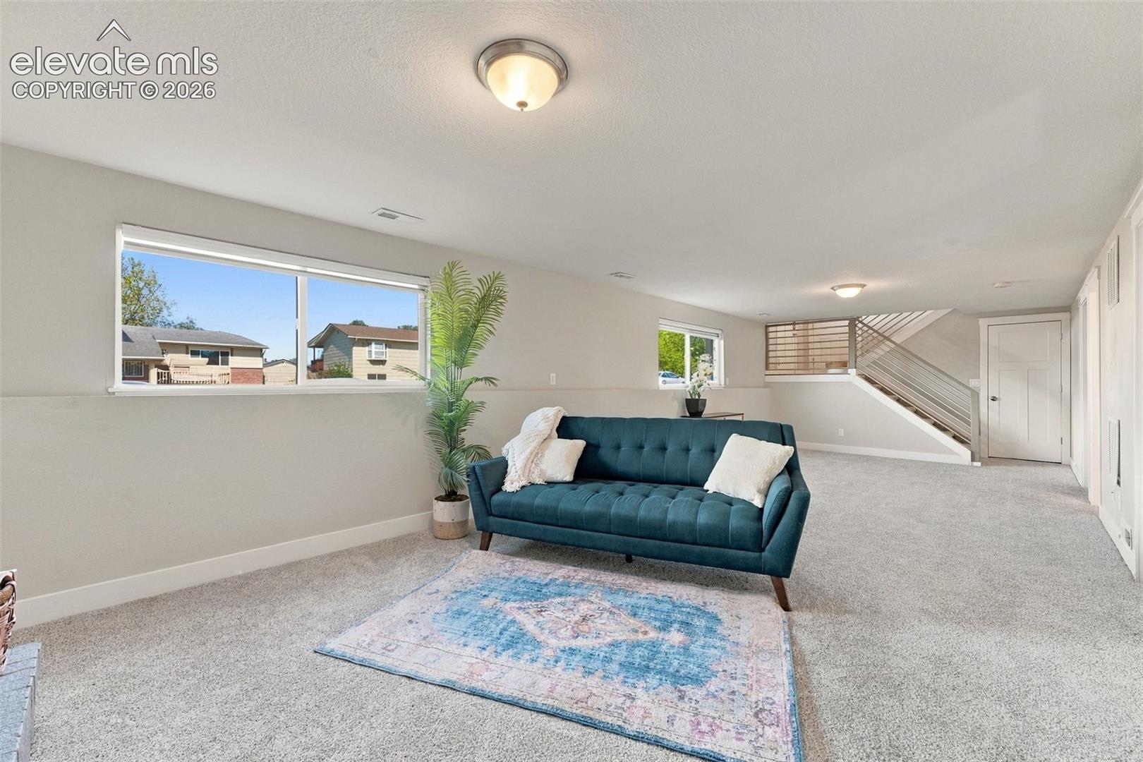 Carpeted living space with multiple windows, recessed ceiling light, and a staircase featuring a modern railing