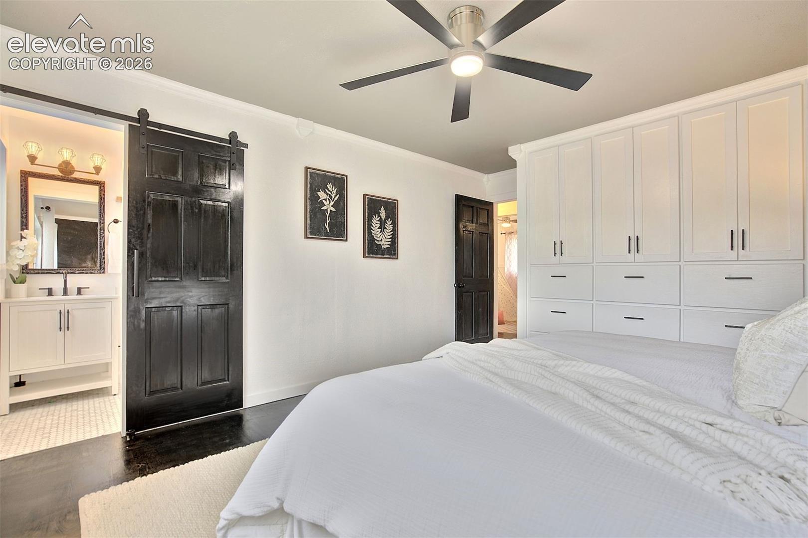Floor-to-ceiling built-in white cabinetry, matte black sliding barn door, dark wood-finish flooring, and a multi-blade ceiling fan with integrated lighting